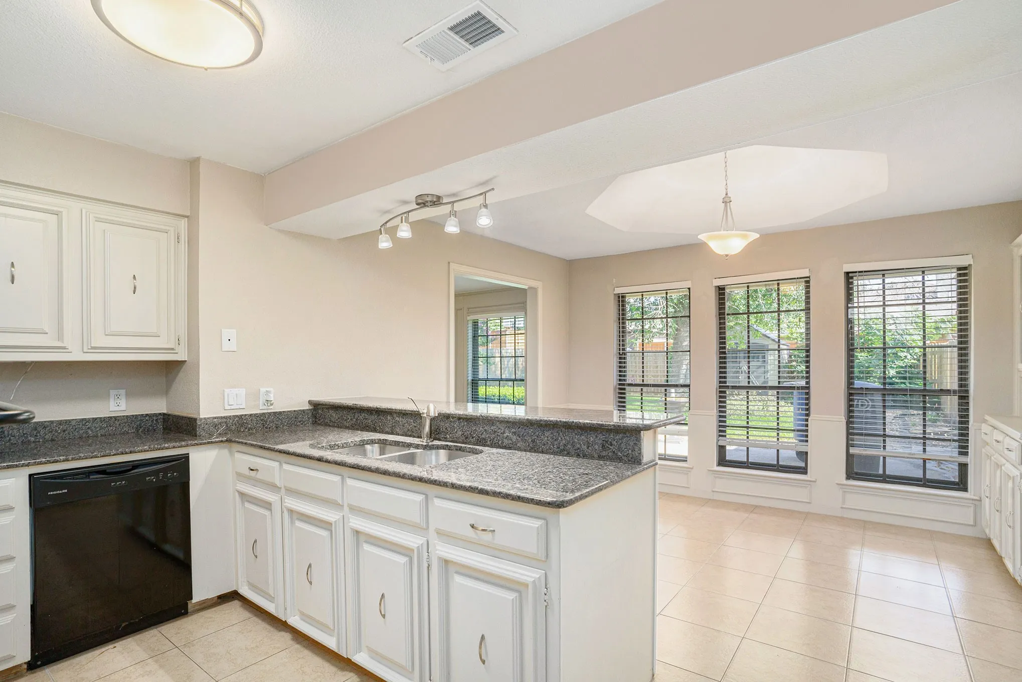 Kitchen with a peninsula, light tile patterned floors, black dishwasher, rail lighting, and white cabinetry