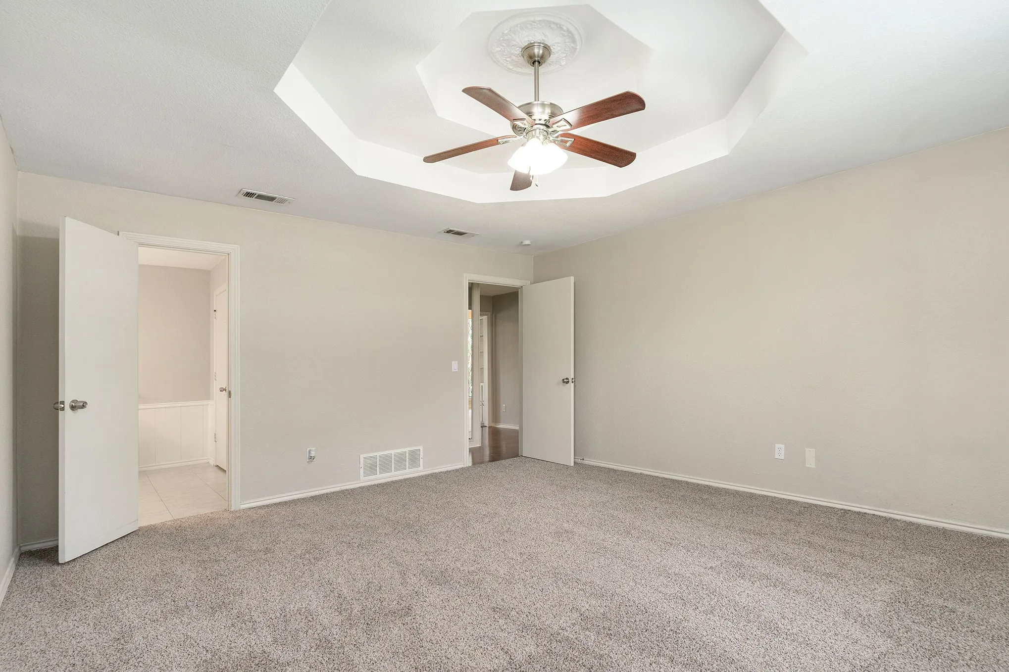 Unfurnished bedroom featuring a tray ceiling, light carpet, ceiling fan, and connected bathroom