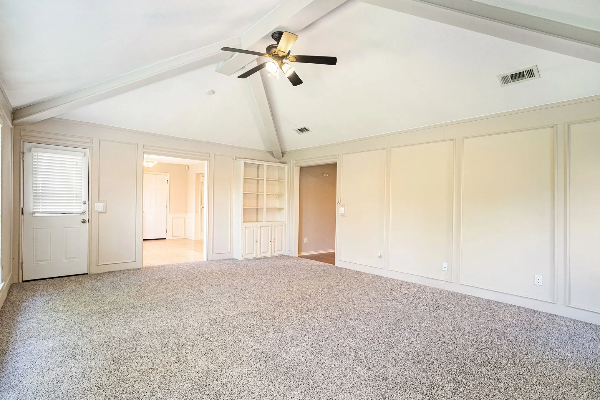 Unfurnished bedroom with beamed ceiling, light carpet, high vaulted ceiling, a decorative wall, and a ceiling fan
