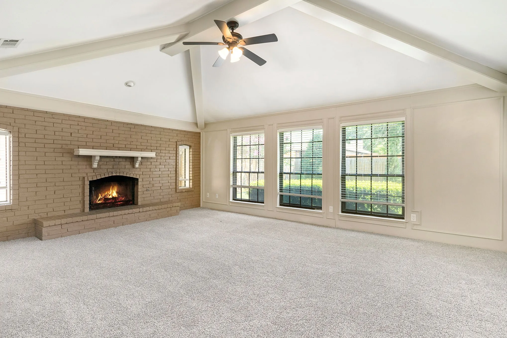 Unfurnished living room with beam ceiling, high vaulted ceiling, carpet, a fireplace, and ceiling fan