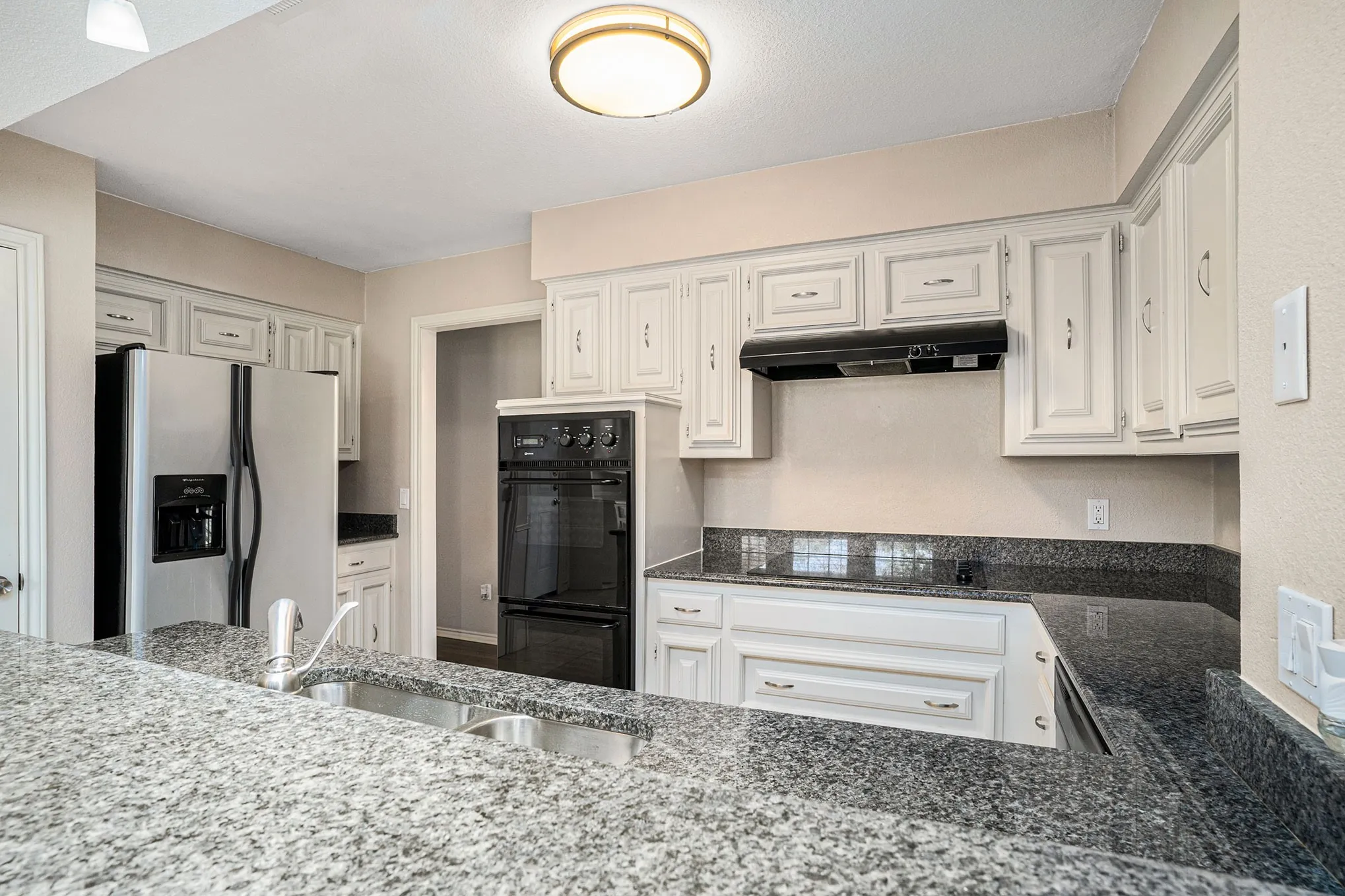 Kitchen featuring stainless steel refrigerator with ice dispenser, dark stone counters, under cabinet range hood, and white cabinetry