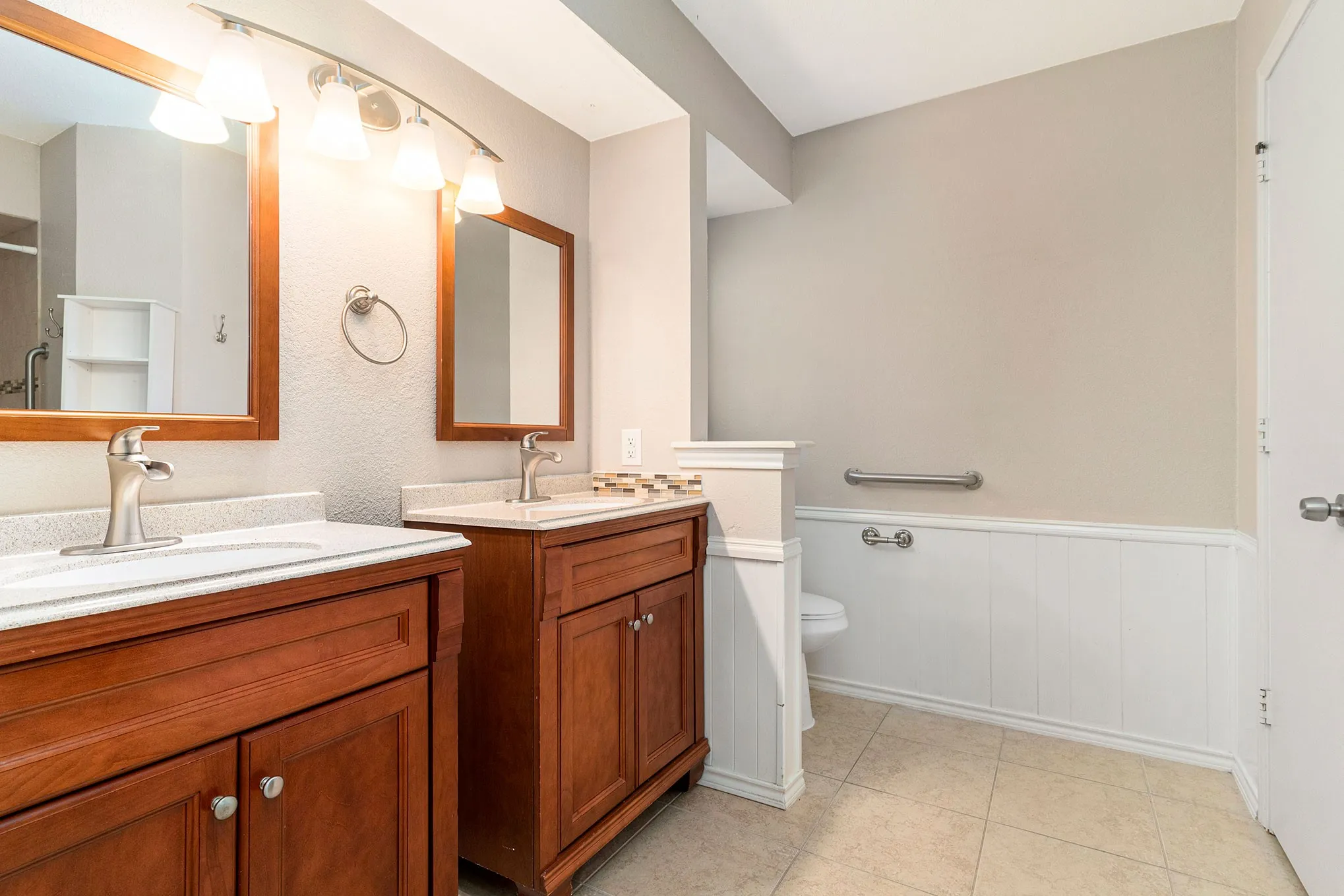 Full bathroom with wainscoting, two vanities, tile patterned floors, and a shower