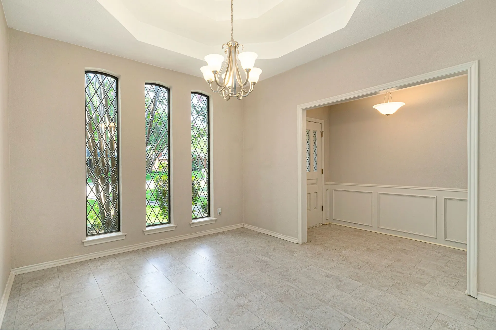 Unfurnished dining area featuring a raised ceiling, a chandelier, and a decorative wall