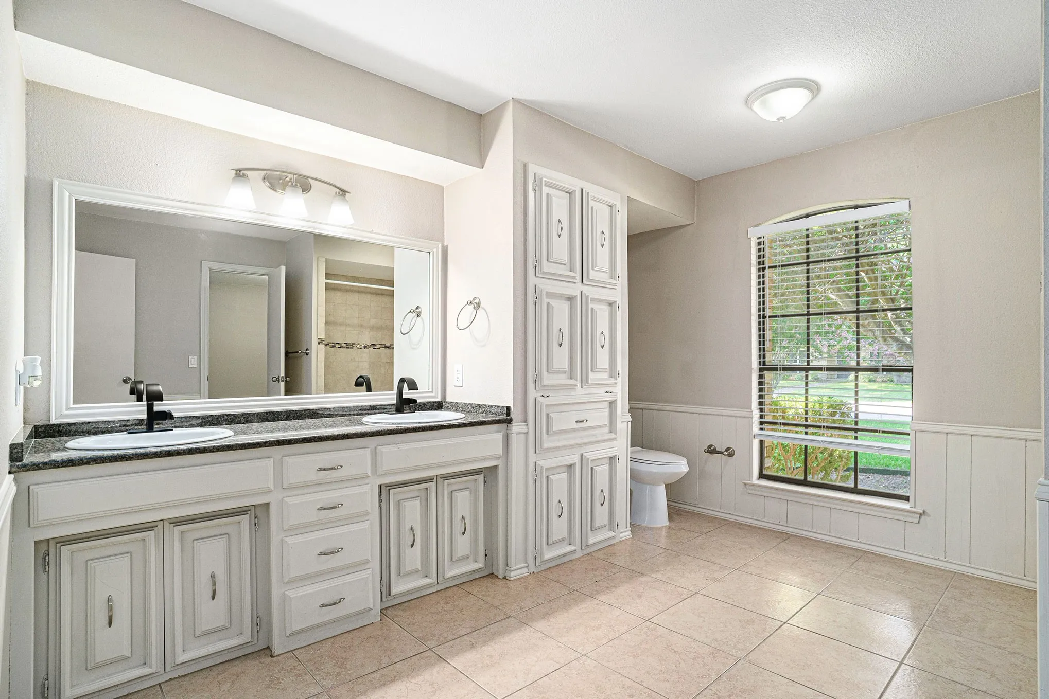 Bathroom featuring wainscoting, double vanity, a tile shower, a decorative wall, and tile patterned flooring