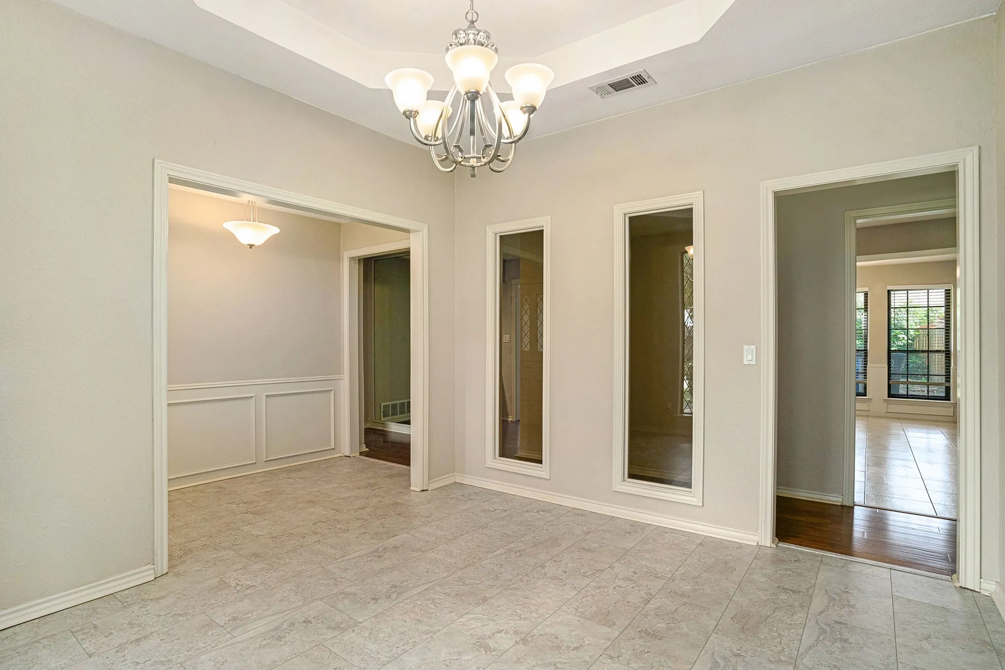 Empty room with a chandelier, a tray ceiling, a decorative wall, and wainscoting
