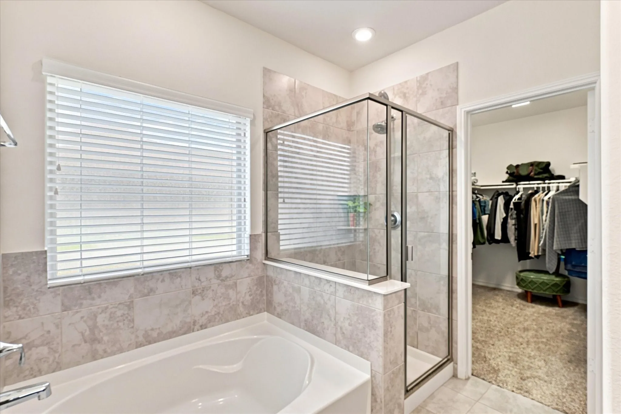 Built-in bathtub, glass-enclosed shower, tiled shower surround, recessed lighting, and a walk-in closet