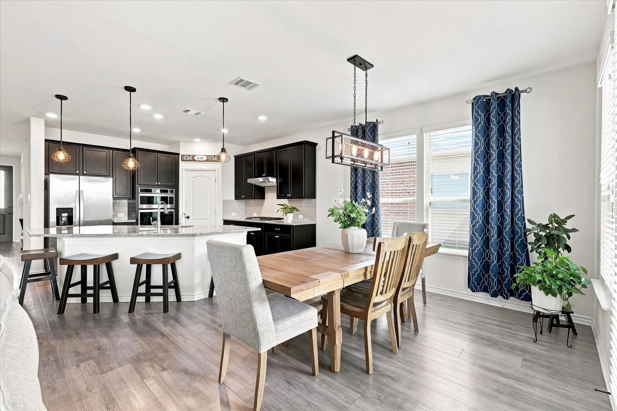 Open-concept living space with wood-finish flooring, a kitchen island with seating, dark wood cabinetry, and stainless steel appliances