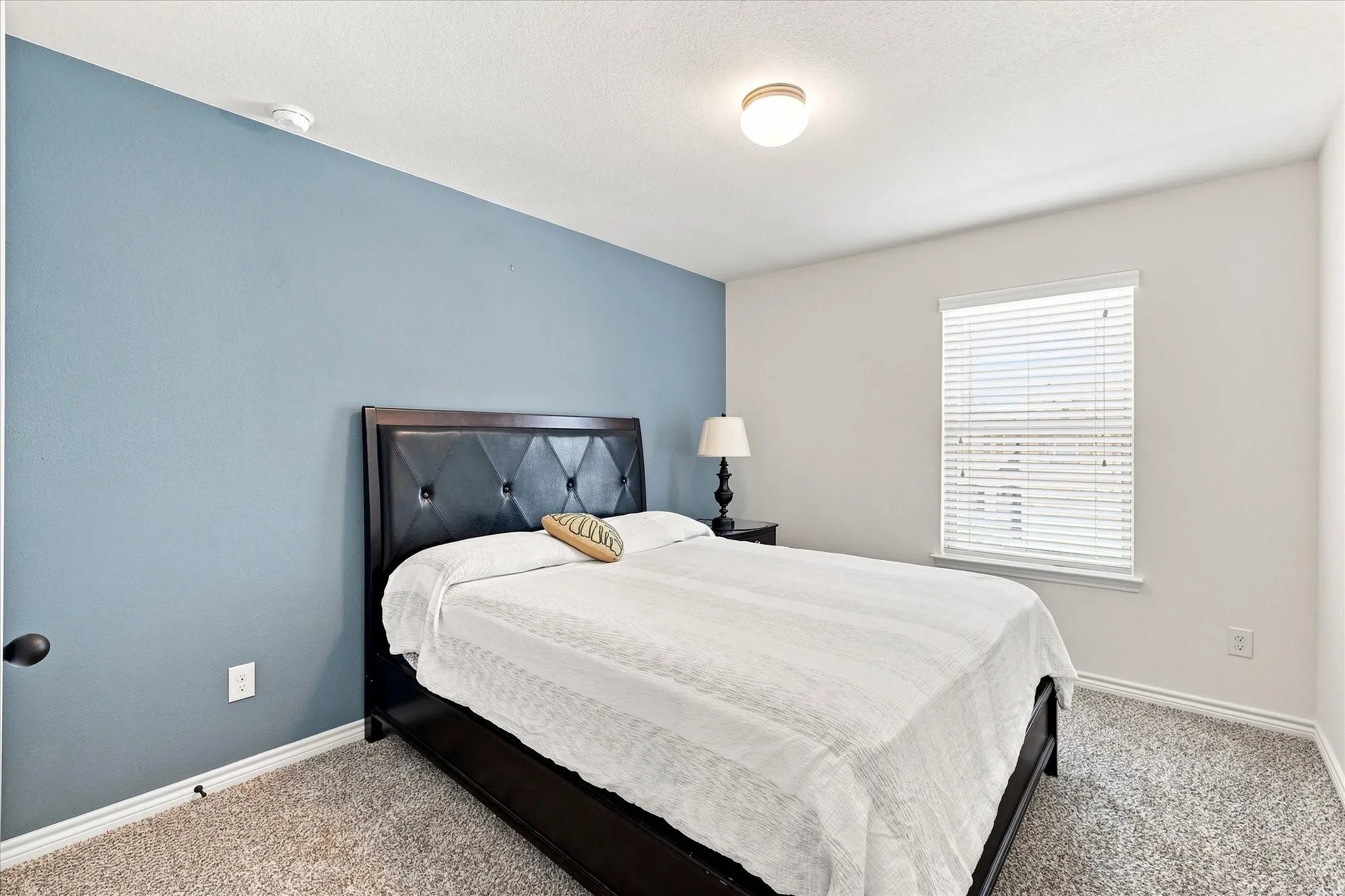 Carpeted flooring, recessed window with blinds, ceiling-mounted light fixture, light-toned wall paint, and an accent wall