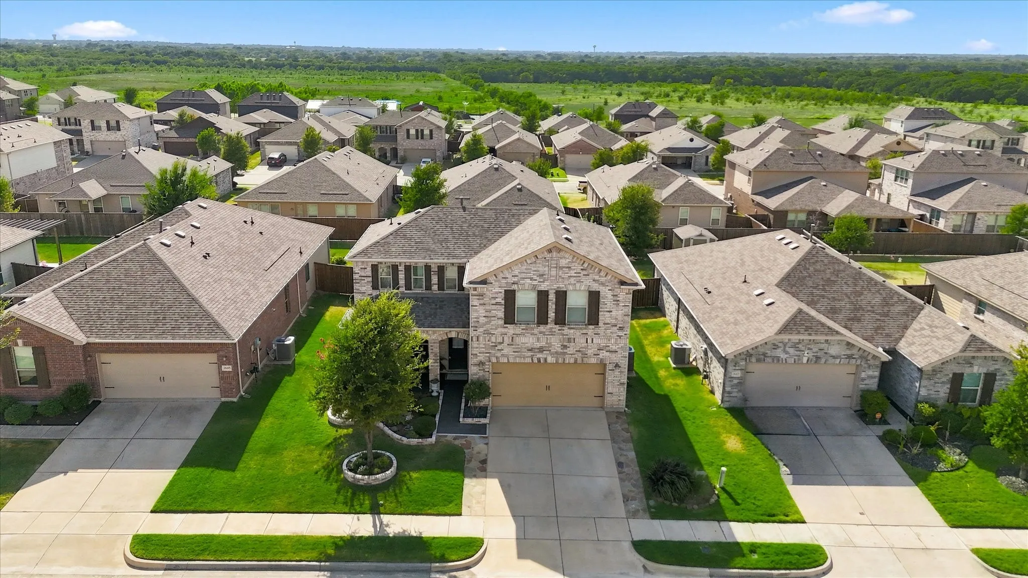 Two-story residence featuring a brick and stone facade, front-facing garage, and mature landscaping