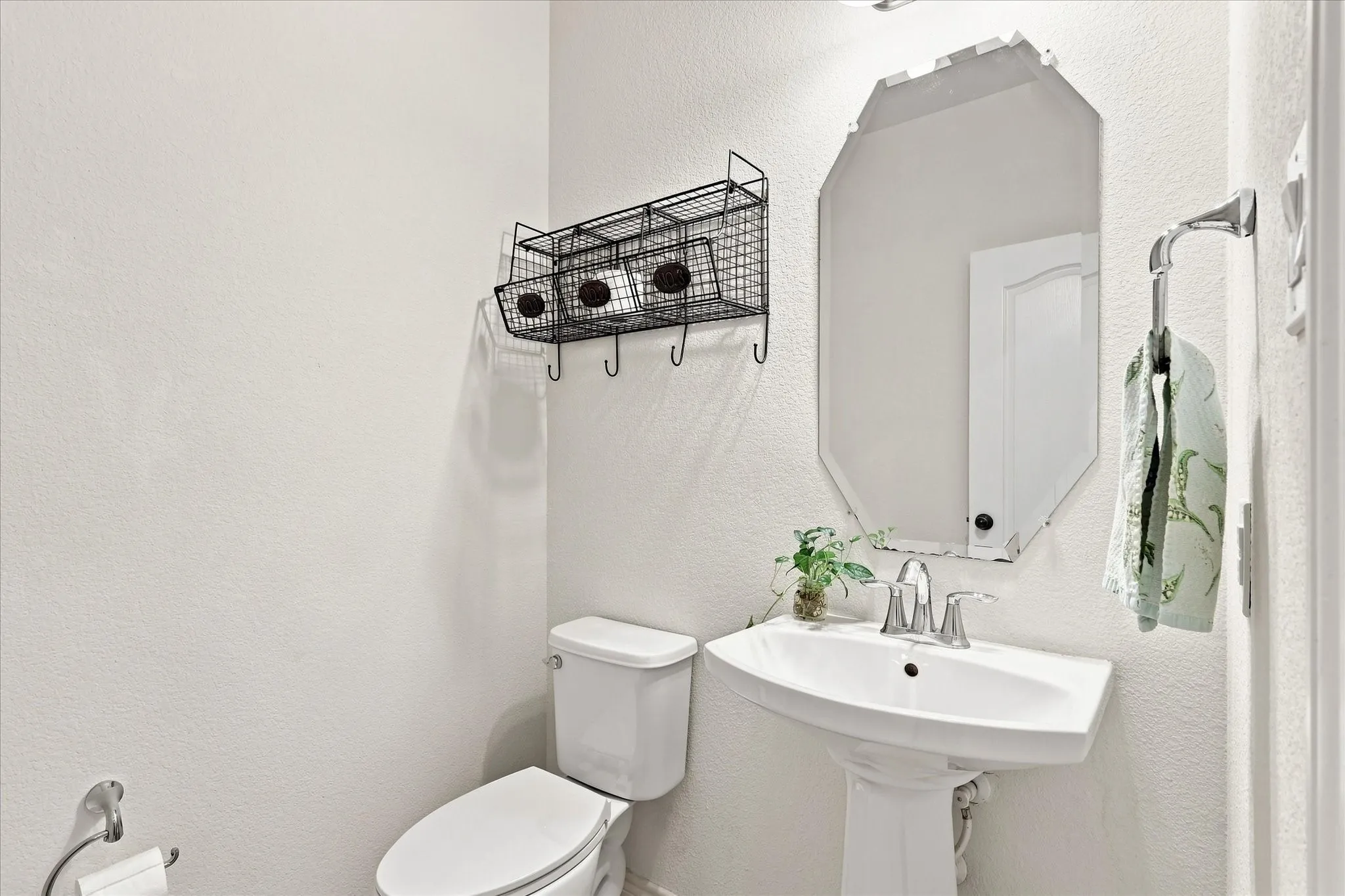 Pedestal sink with chrome faucet, wall-mounted mirror, and white toilet