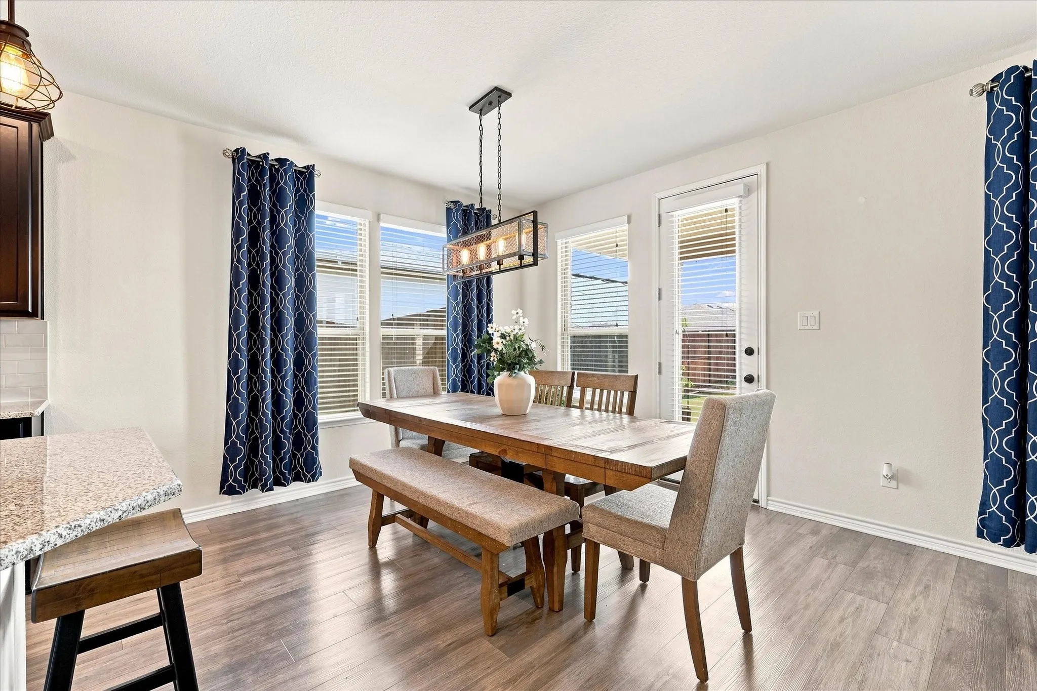 Wood-finish flooring, multiple windows with blinds, a modern linear chandelier, and a built-in countertop with an overhang