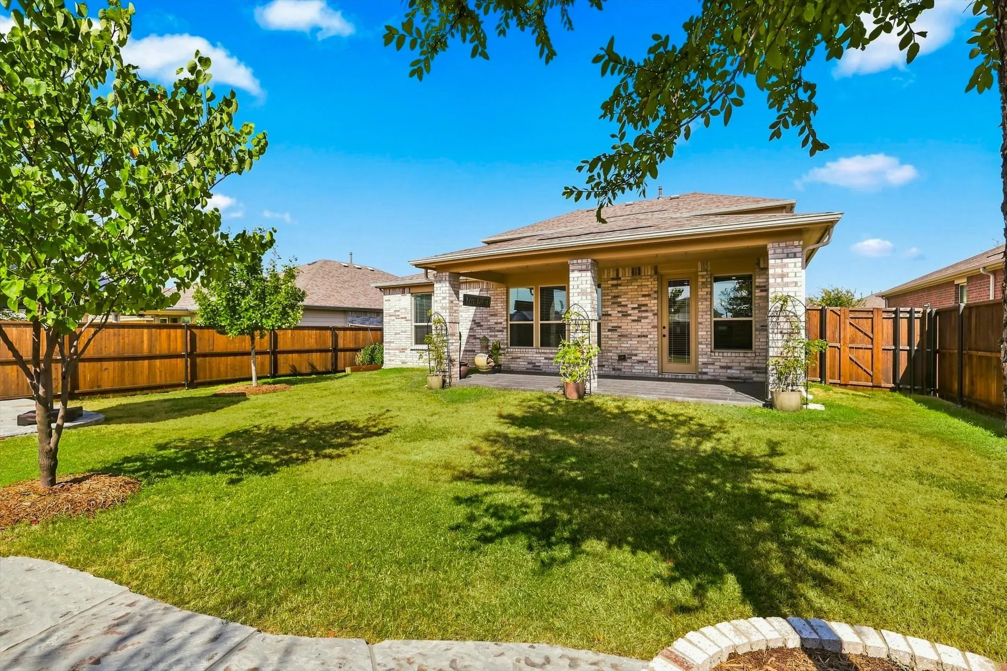 Expansive backyard featuring a covered patio, brick exterior, and a wood privacy fence