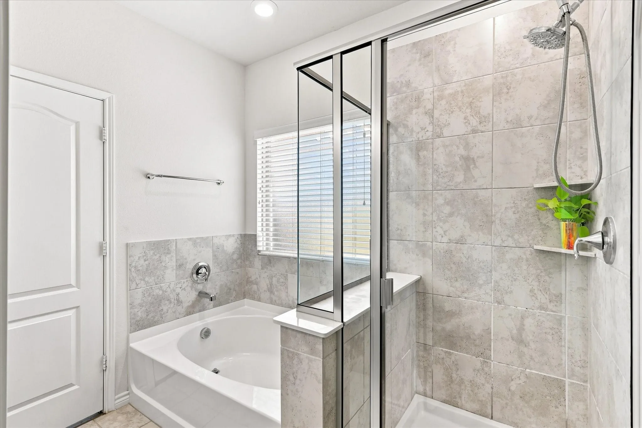 Spacious bathroom featuring a built-in soaking tub, a separate glass-enclosed shower with a handheld showerhead, and tile-surround walls