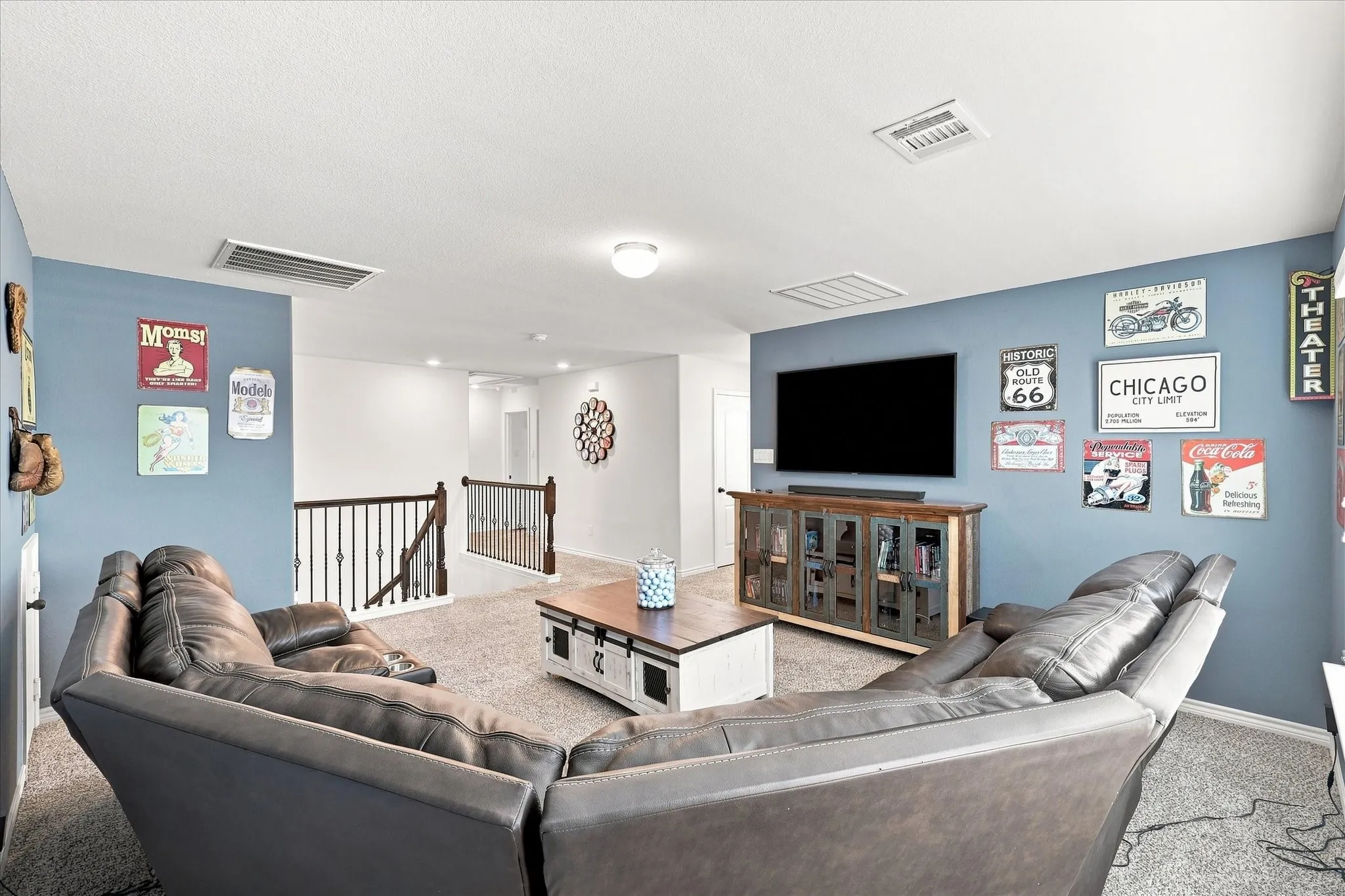 Spacious upper-level area featuring a media console with glass panel doors, carpet flooring, and a railing with metal spindles