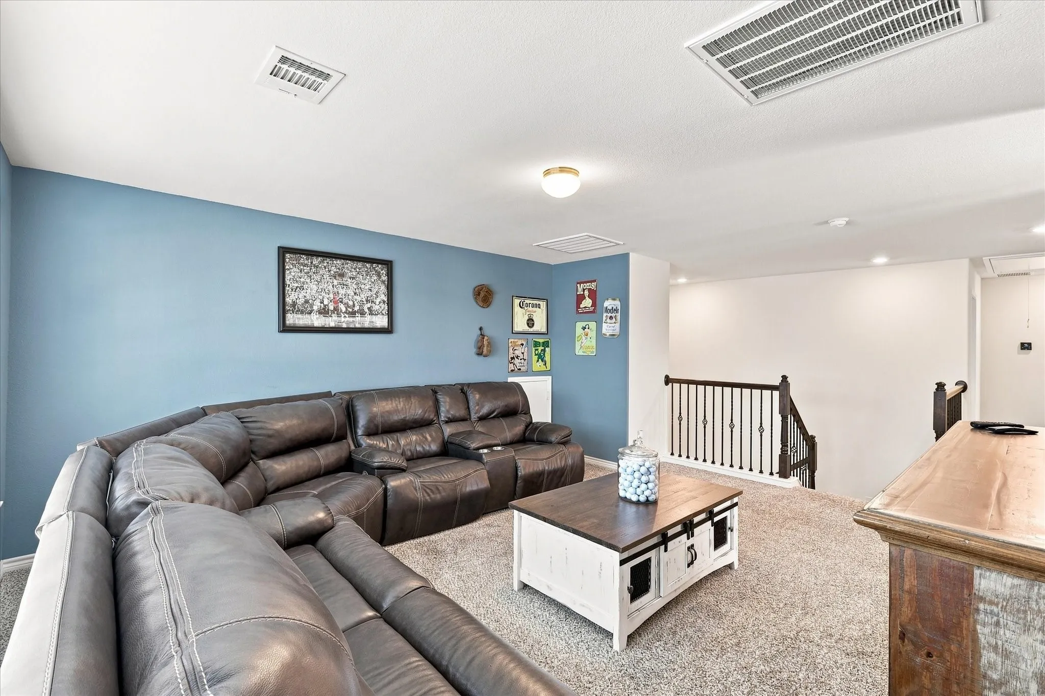 Carpeted entertainment area with a partial staircase, metal balusters, and a wooden handrail