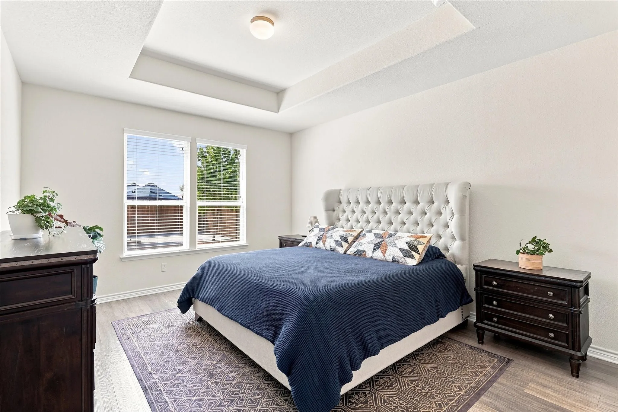 Tray ceiling with recessed lighting, dual windows with blinds, wood-finish flooring, and light-toned walls