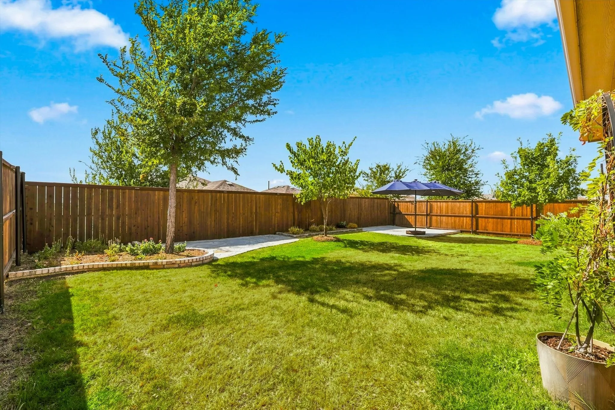 Expansive backyard featuring a manicured lawn, full privacy fencing, established trees, and a concrete patio