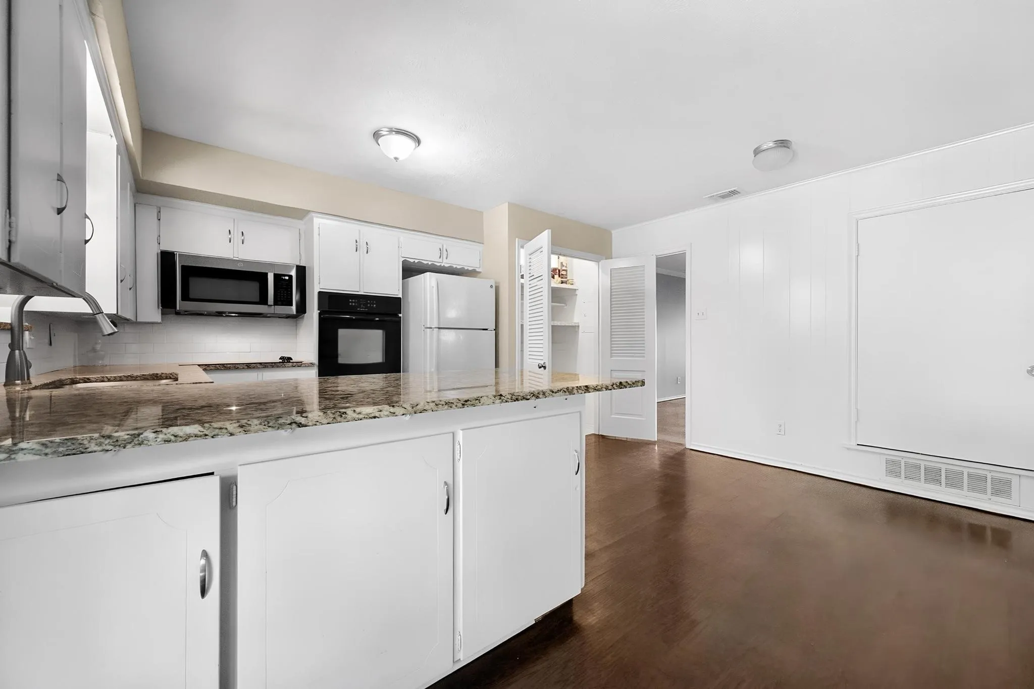 Kitchen featuring white cabinetry, stone countertops, stainless steel microwave, and wood-finish flooring