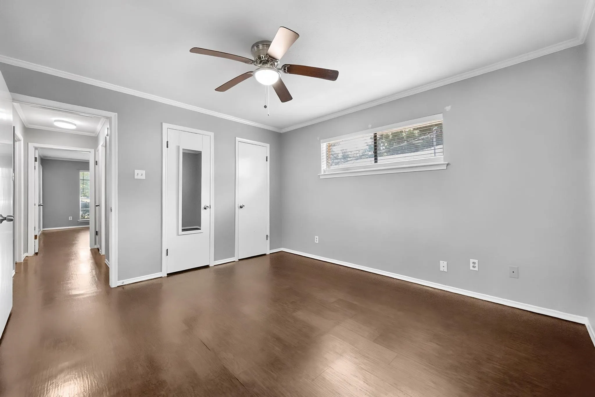 Spacious bedroom showcasing rich wood-finish flooring, neutral wall finishes, and abundant natural light from transom window
