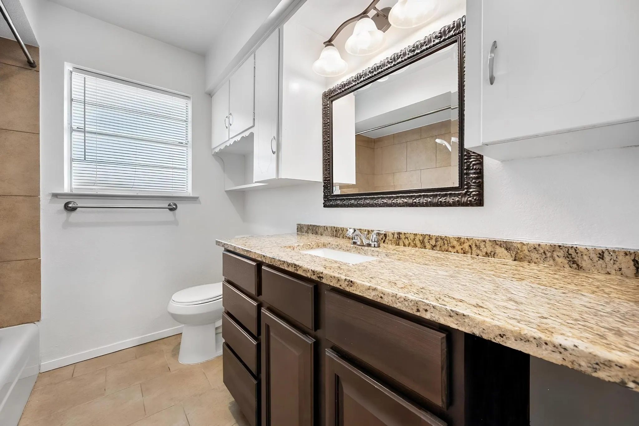 Bathroom featuring a vanity with a light-toned countertop, dark wood-finish cabinetry, and an ornate framed mirror