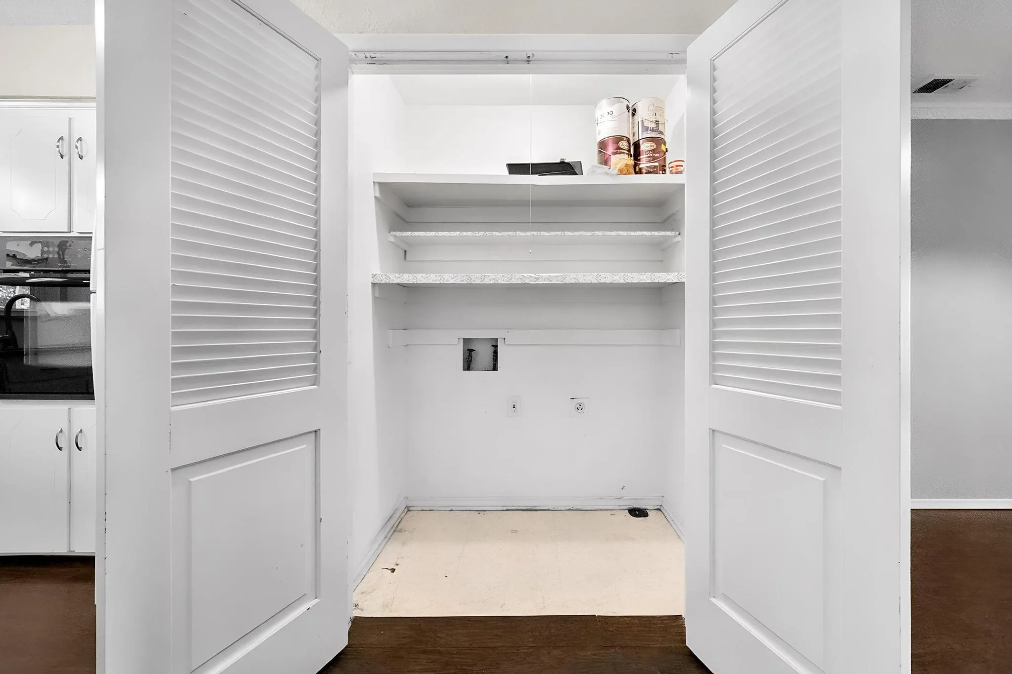 Dedicated pantry with louvered bi-fold doors, two shelves, and wood-finish flooring