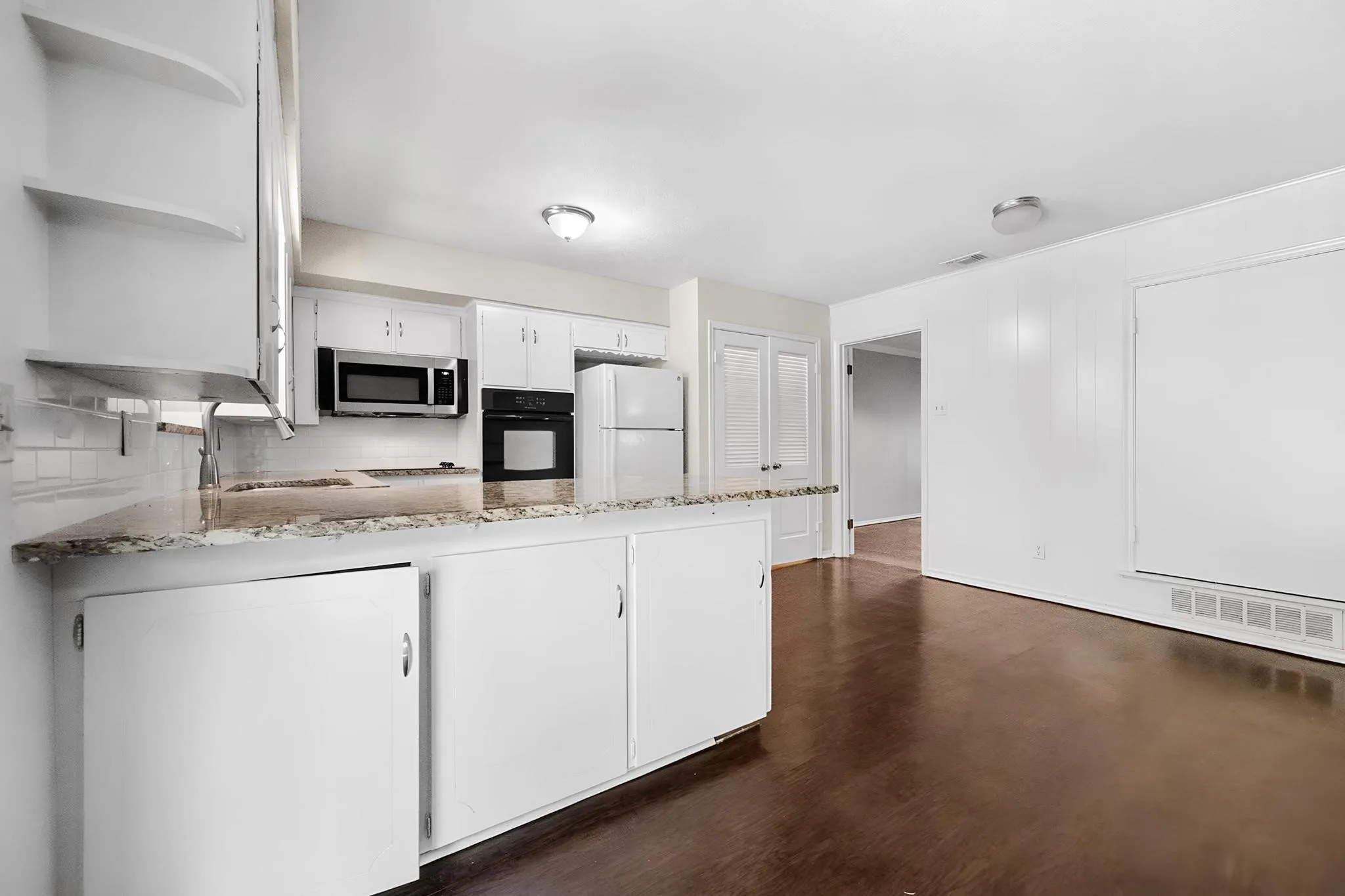 Kitchen featuring white cabinetry, built-in microwave, dark wood-finish flooring, and white appliances