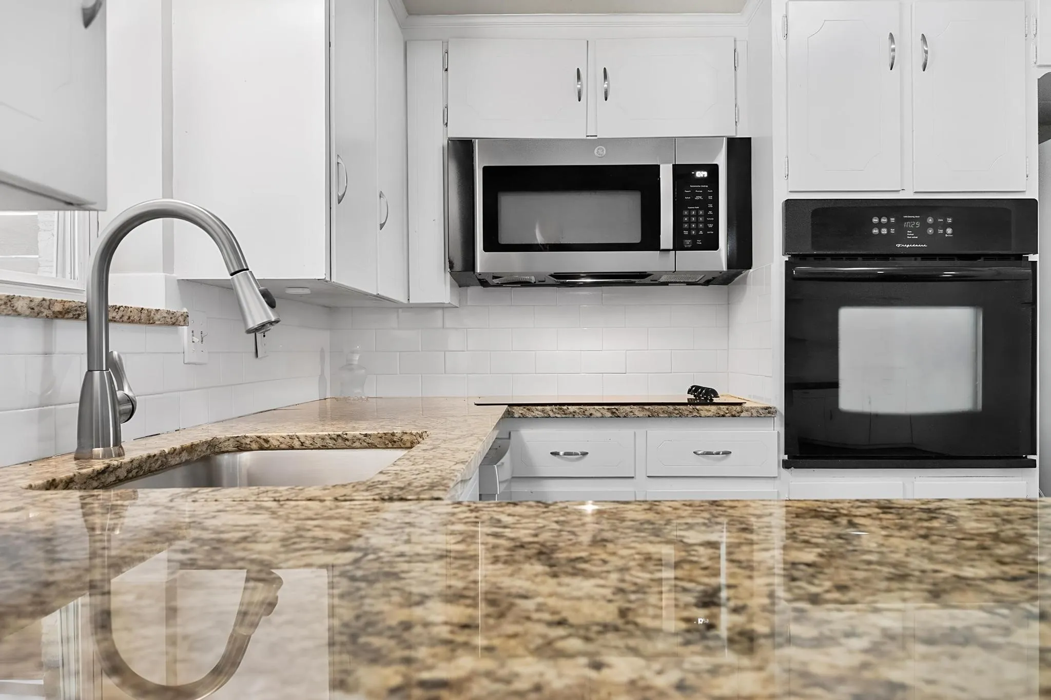 Granite-patterned countertops, stainless steel sink, subway tile backsplash, white cabinetry, and stainless steel microwave