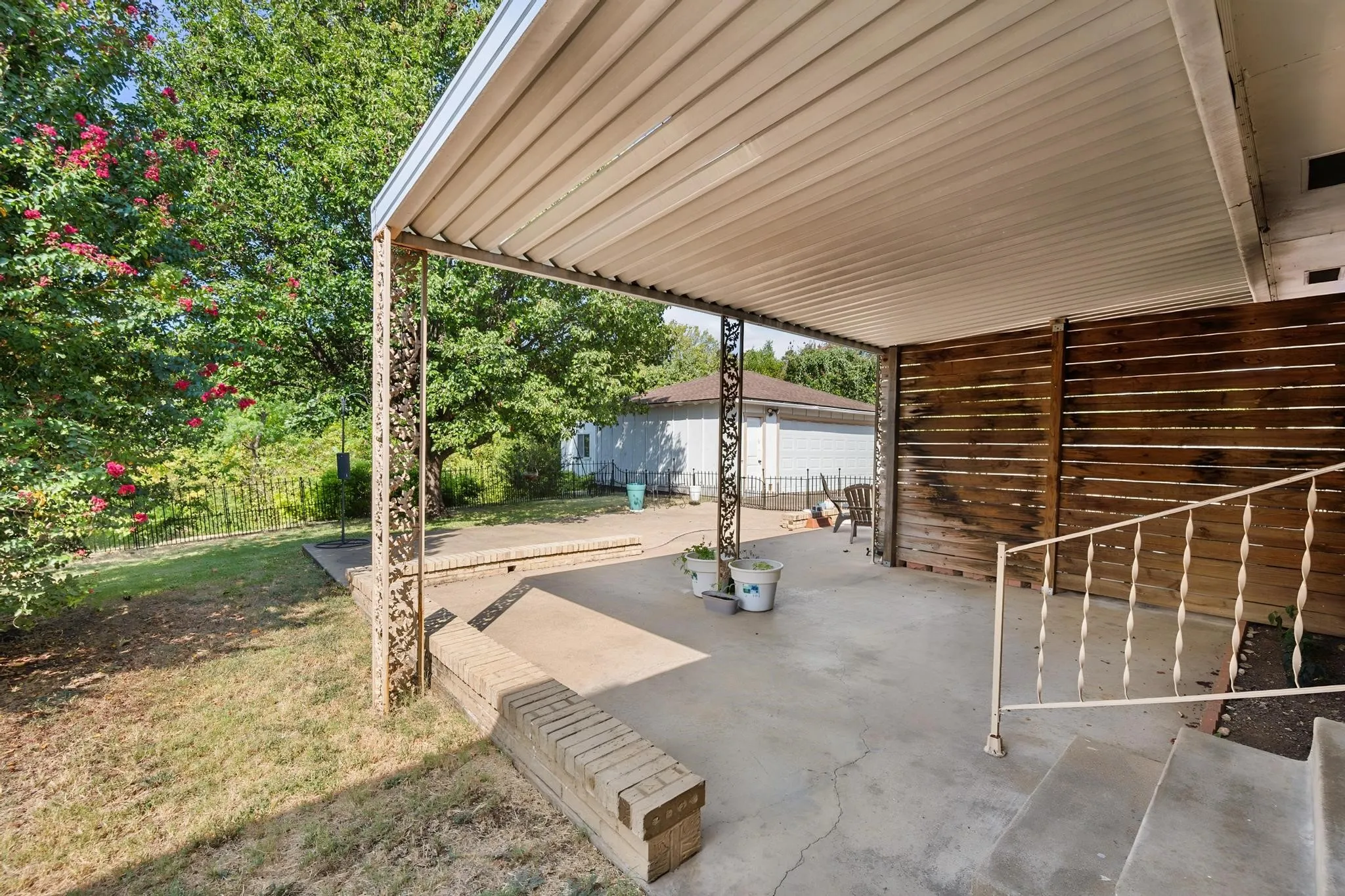 Covered patio featuring concrete flooring, decorative metal supports, and a horizontal wood privacy screen