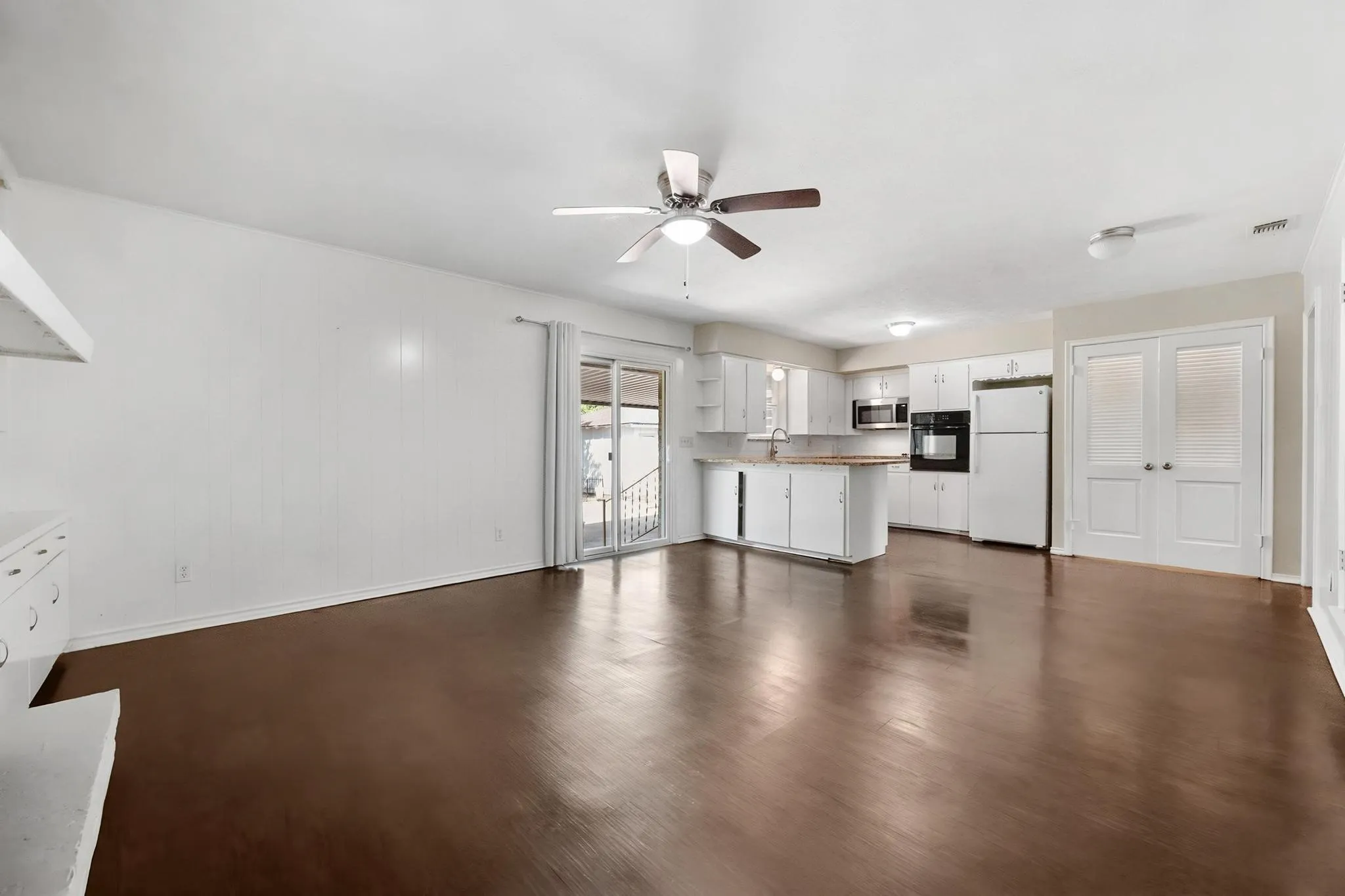 Expansive room featuring wood-finish flooring, a ceiling fan, and white cabinetry