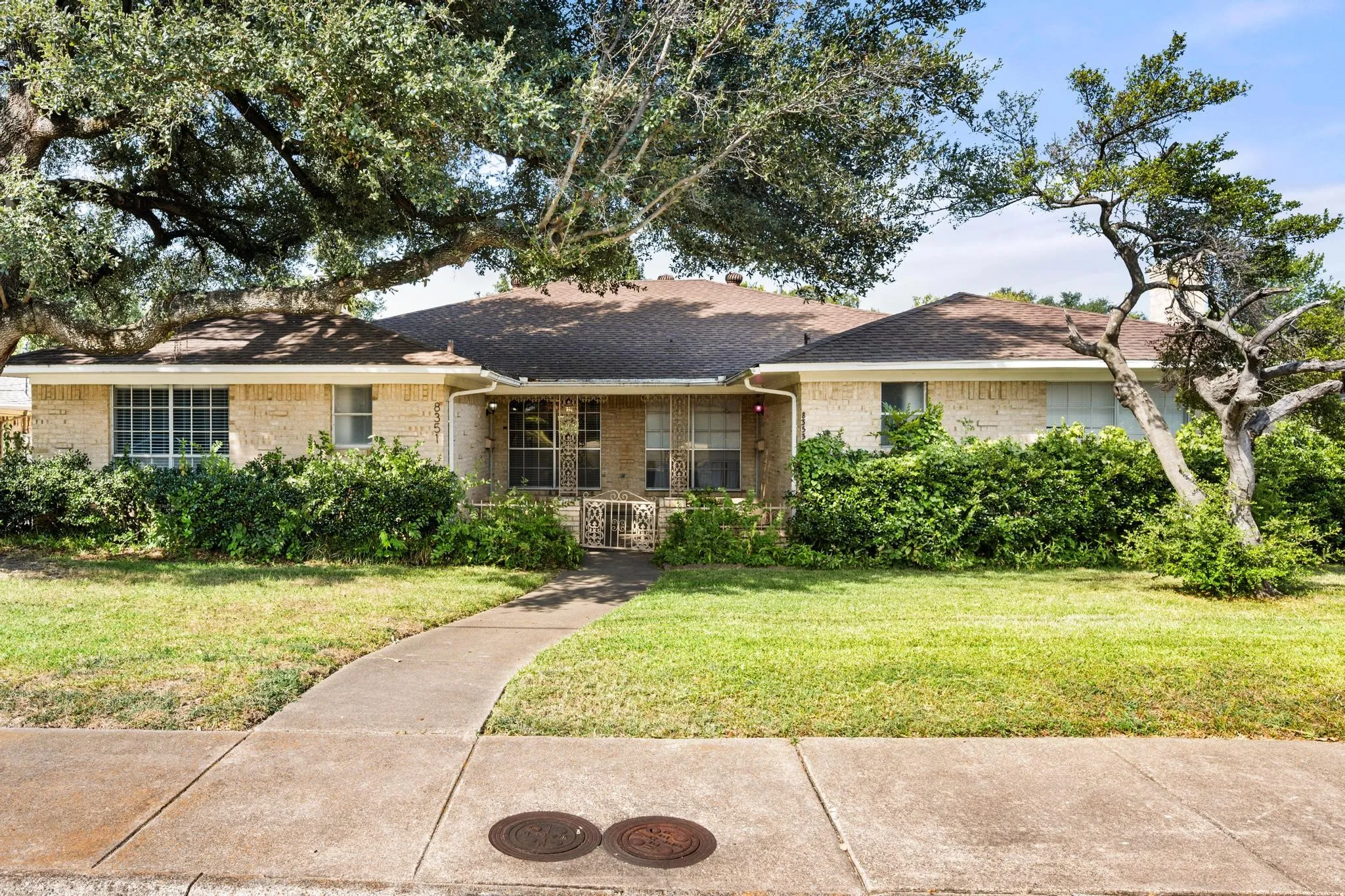Brick exterior with a shingle roof and mature trees framing the property
