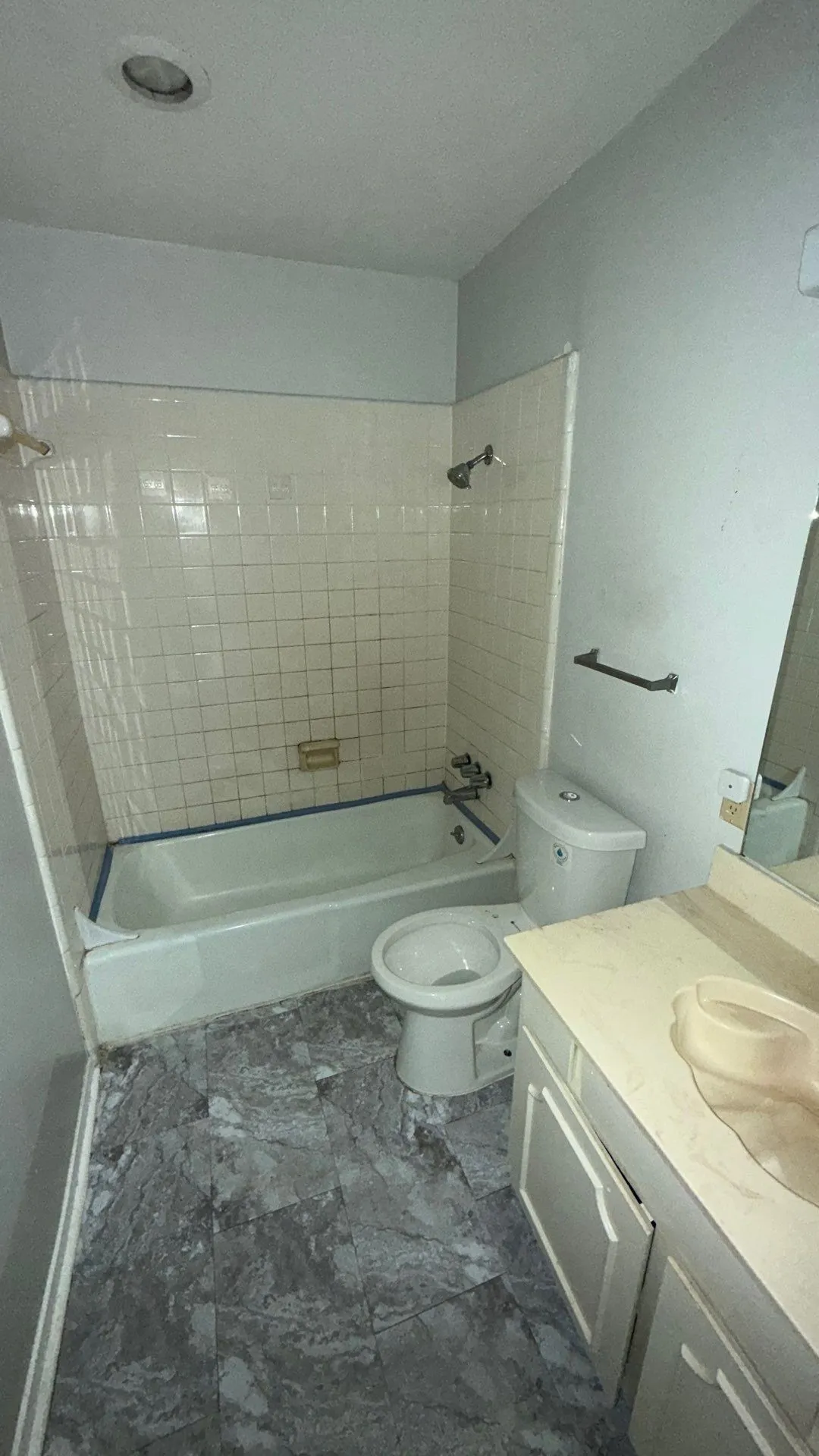 Bathroom featuring a bathtub with subway tile surround, a toilet, a vanity with an integrated sink, and patterned floor tiling