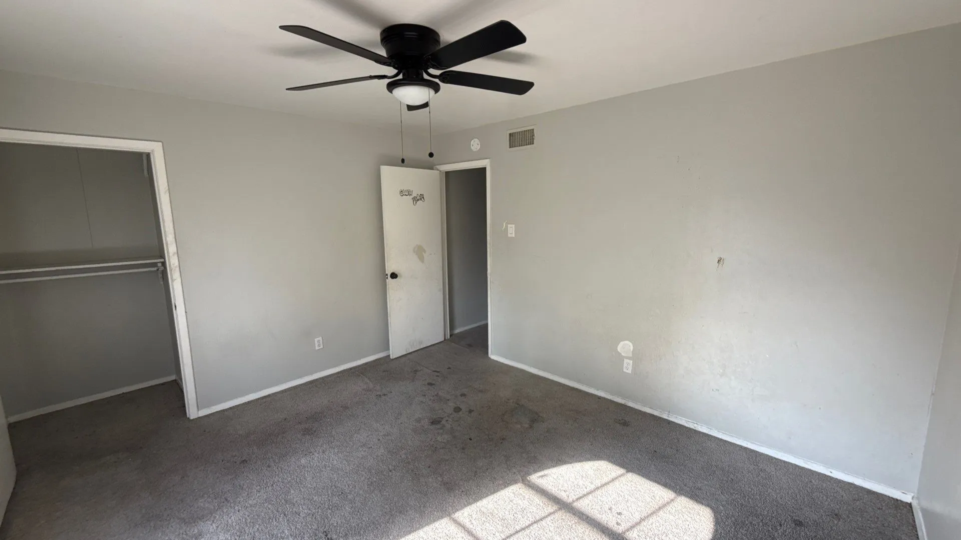 Ceiling fan with integrated lighting, neutral wall paint, open closet with hanging rod, flush-mounted door, and grey carpet flooring