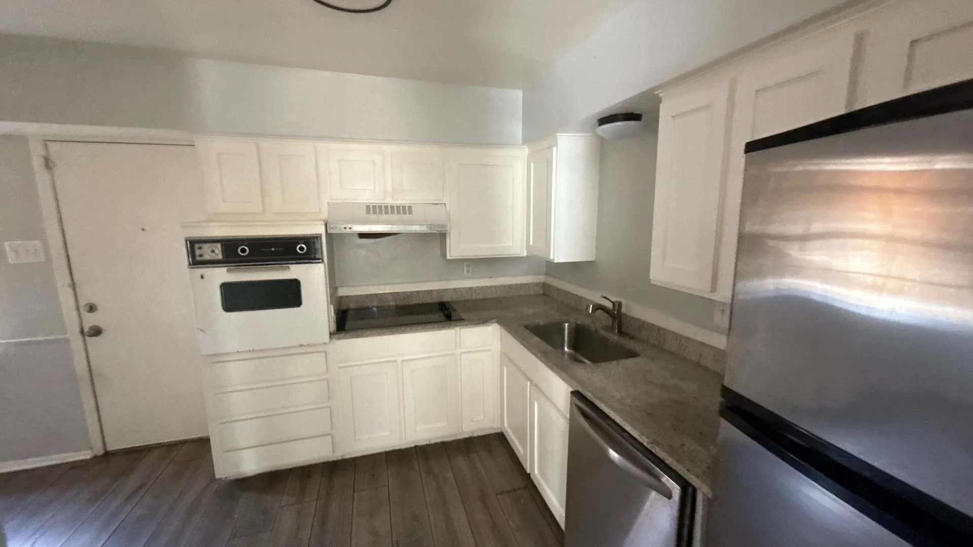 Kitchen featuring wood-finish flooring, white cabinetry, granite-style countertops, stainless steel appliances, and an integrated oven