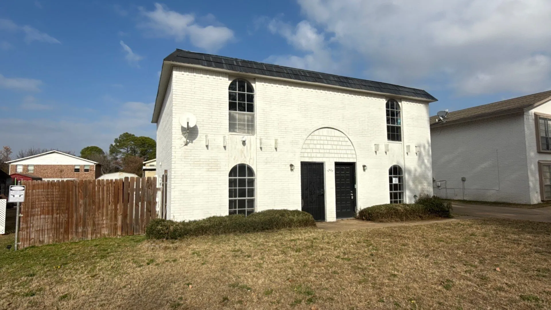 White brick exterior featuring arched windows and dark entry doors