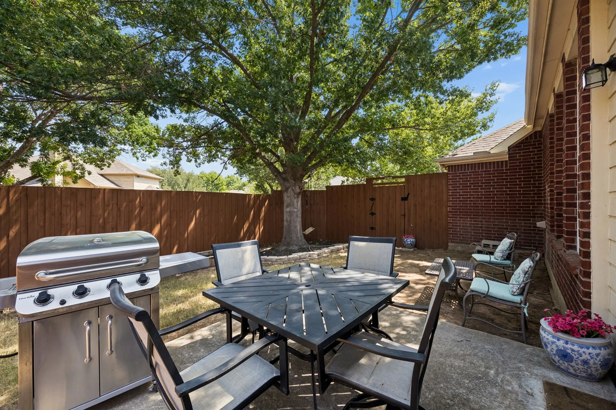 Private concrete patio with a full privacy fence, mature trees, and a brick exterior