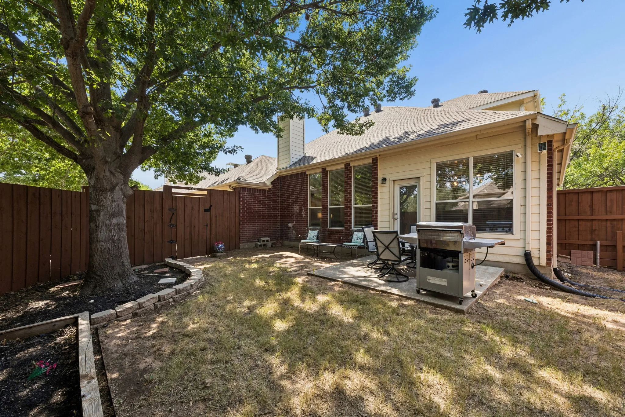 Paved patio area, brick exterior accent, siding, privacy fencing, and mature trees