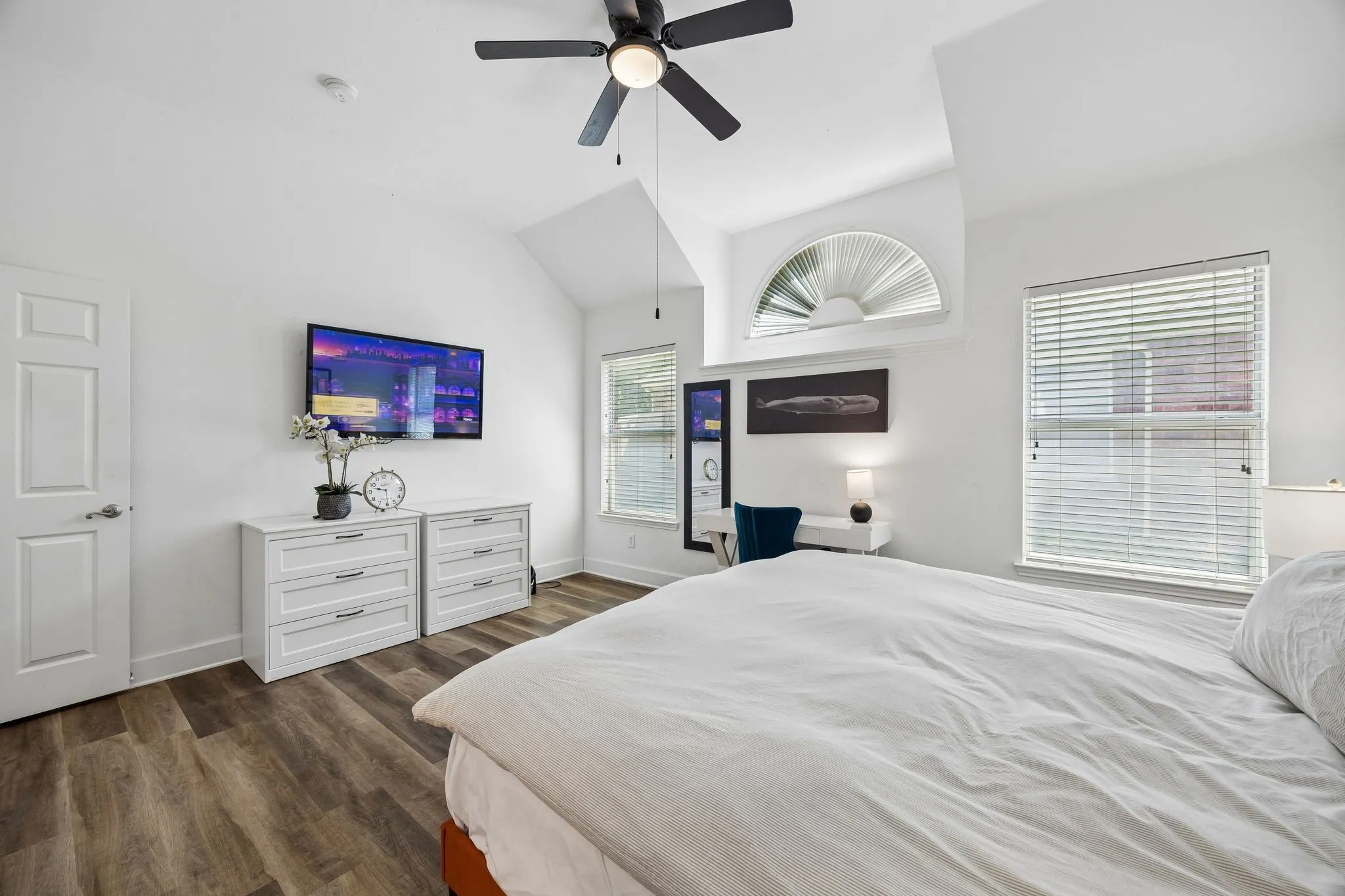Vaulted ceiling with a ceiling fan, wood-finish flooring, multiple windows with blinds, and an arched transom window