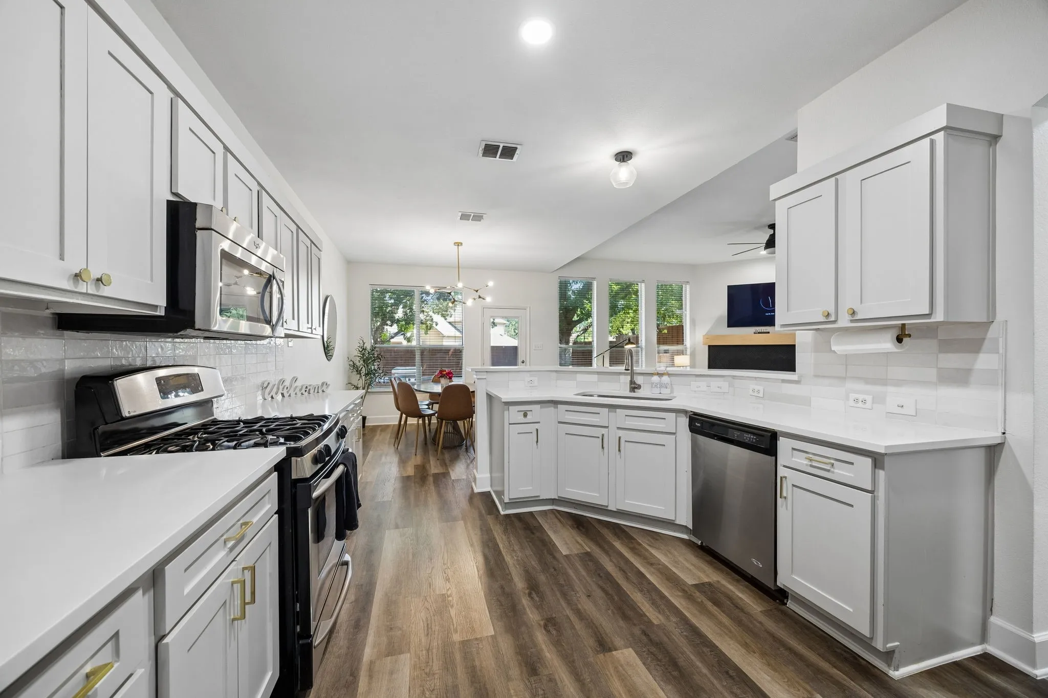 Kitchen featuring wood-finish flooring, white cabinetry with gold-tone hardware, white countertops, and stainless steel appliances