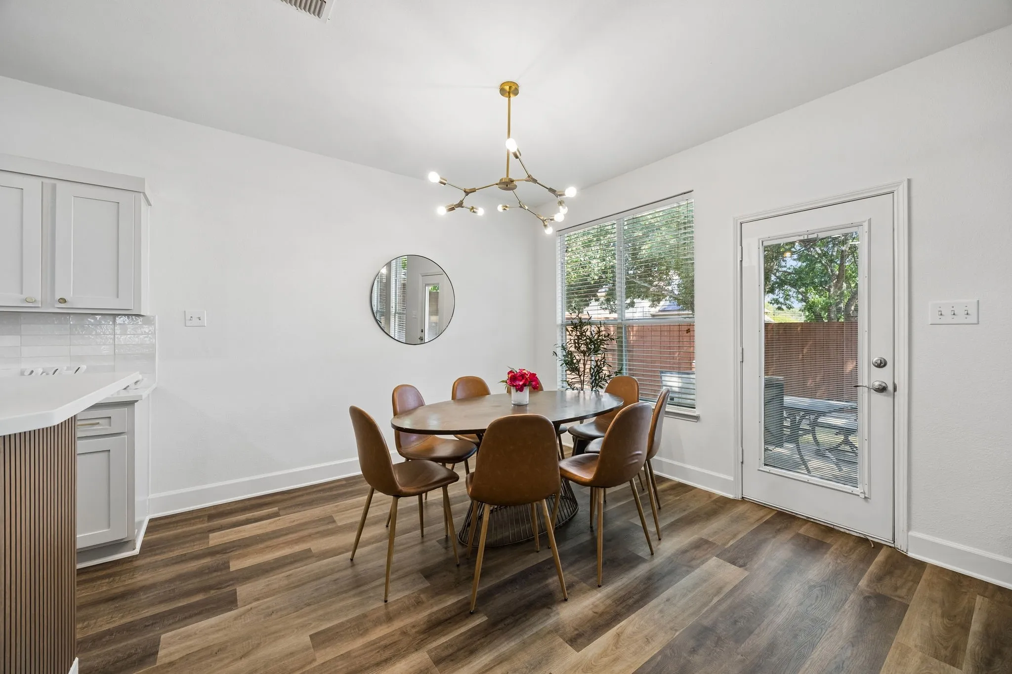 Wood-finish flooring throughout, bright white walls, modern ceiling light fixture, kitchen cabinetry with subway tile backsplash, and a full-light exterior door