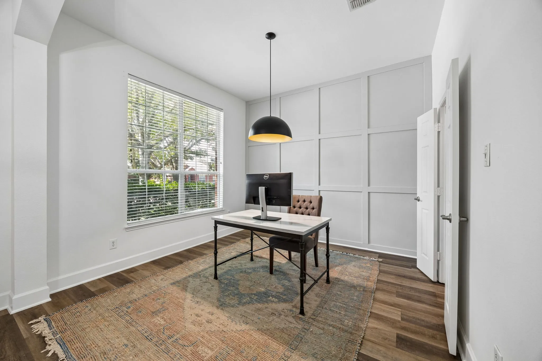 Wood-finish flooring, accent panel wall, large window with blinds, and a pendant light fixture