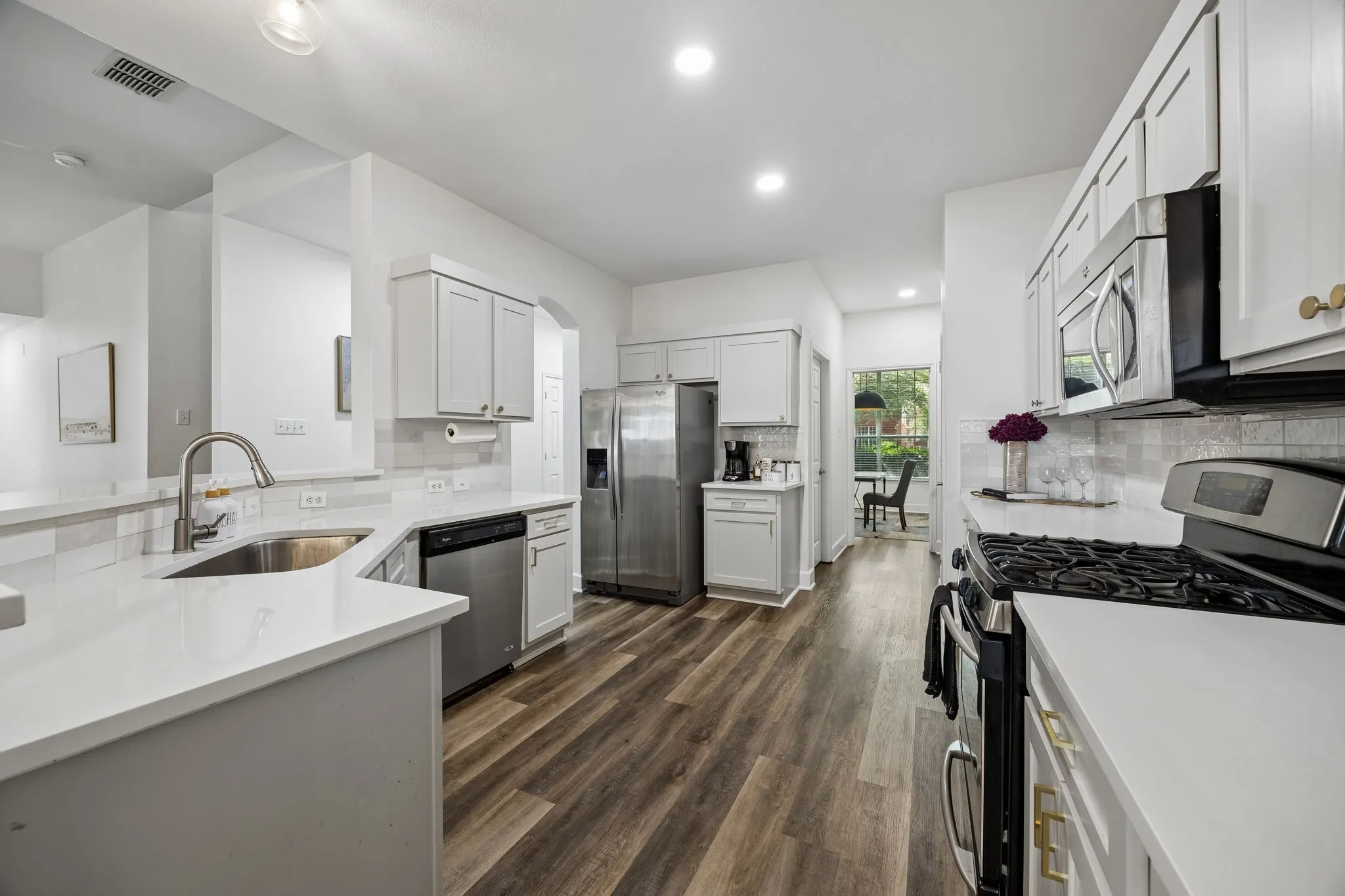 Contemporary kitchen featuring white cabinetry, stainless steel appliances, wood-finish flooring, white countertops, and a subway tile backsplash