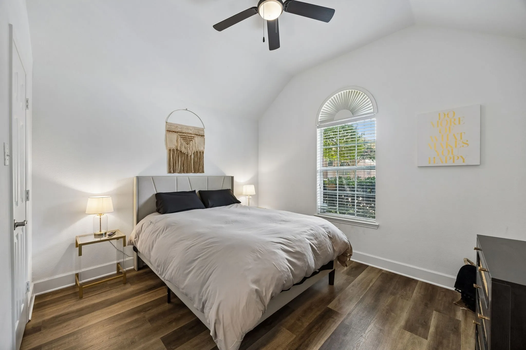Vaulted ceiling, wood-finish flooring, arched window, ceiling fan with integrated lighting, and white walls