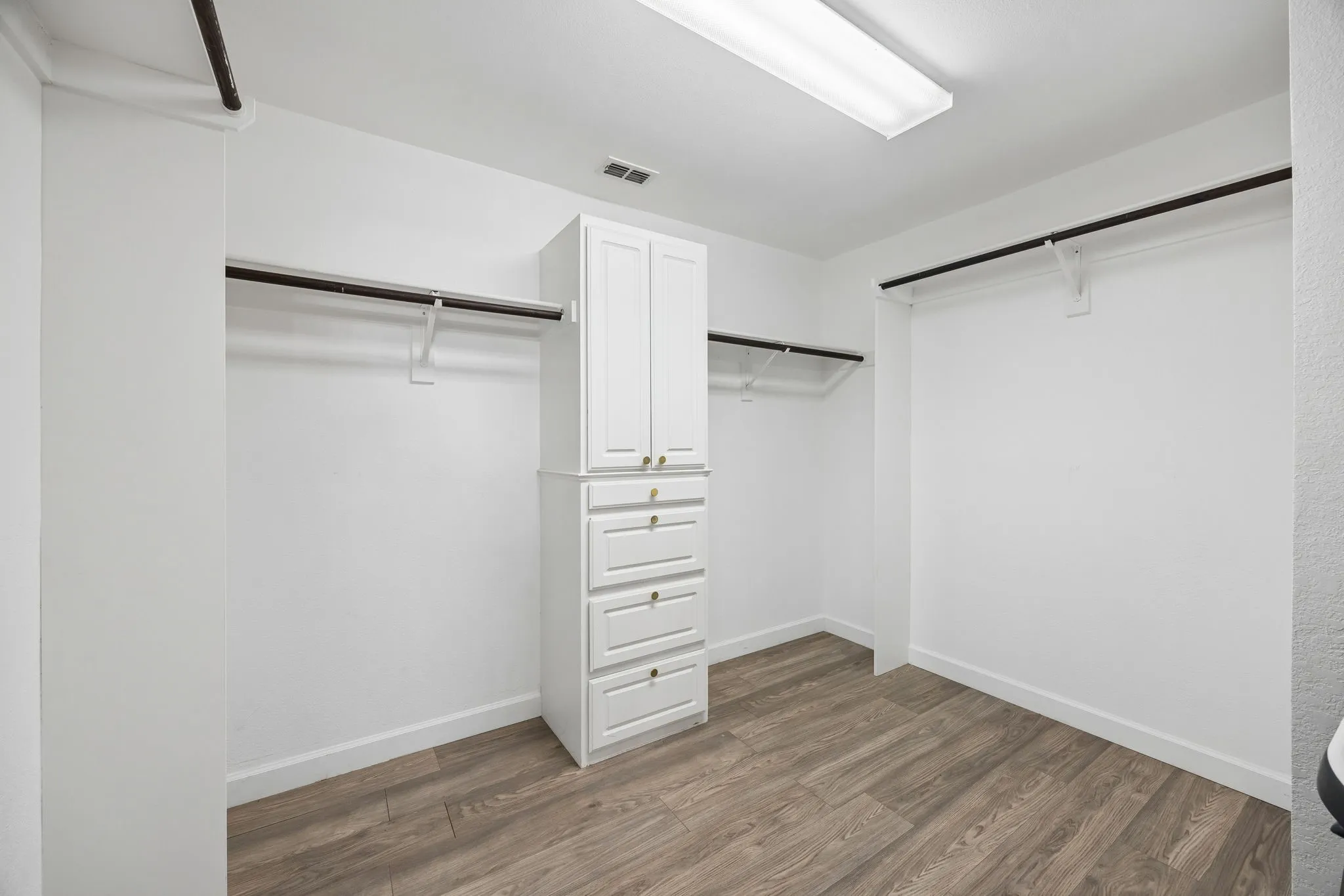 Custom built-in storage cabinetry with drawers, wood-finish flooring, and ample hanging space