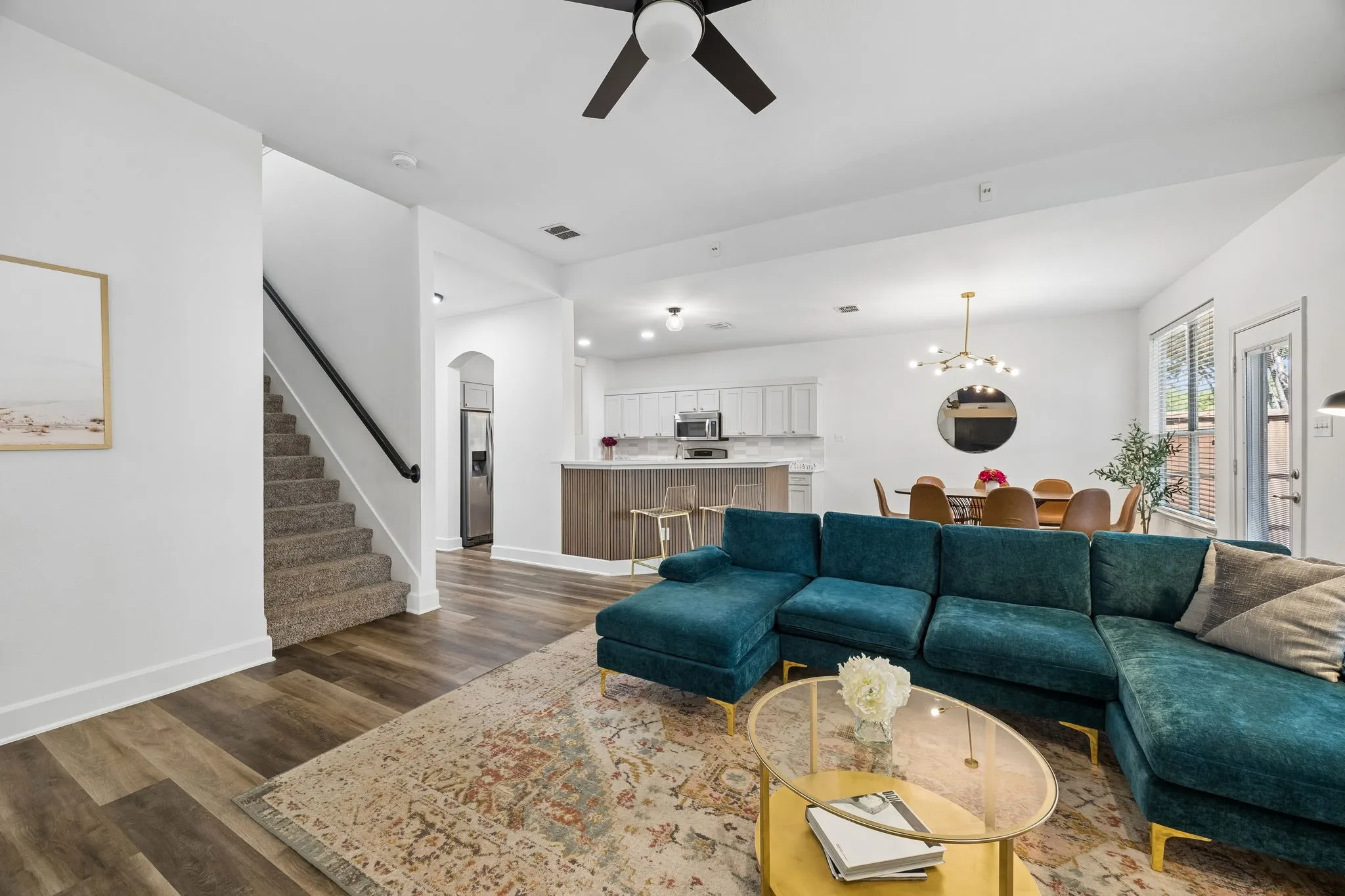 Open-concept living space featuring wood-finish flooring, a contemporary ceiling fan, and a carpeted staircase with a black handrail
