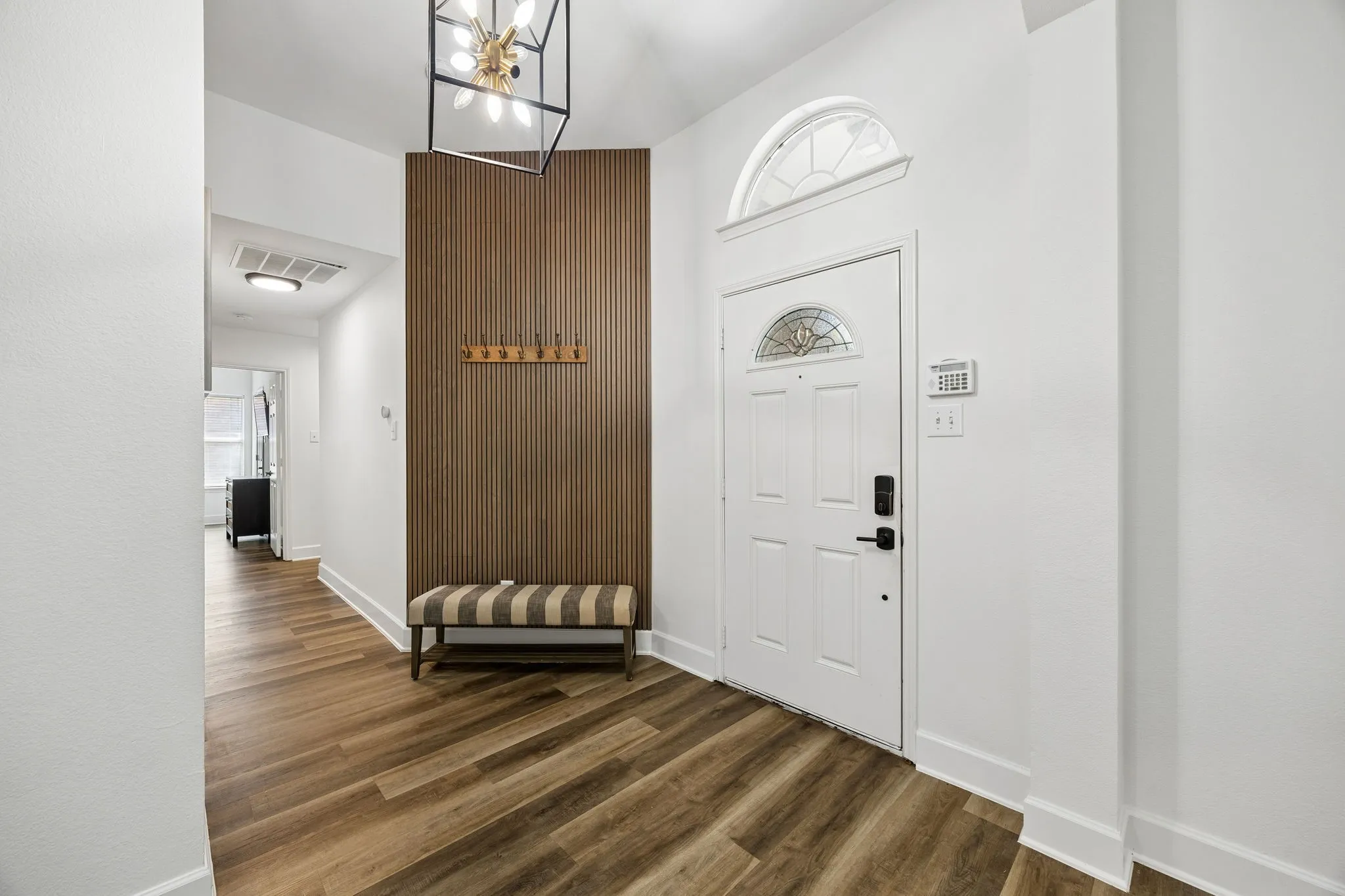 Entryway featuring wood-finish flooring, a white paneled door with an arched transom, a decorative ceiling light fixture, and a vertical wood slat accent wall