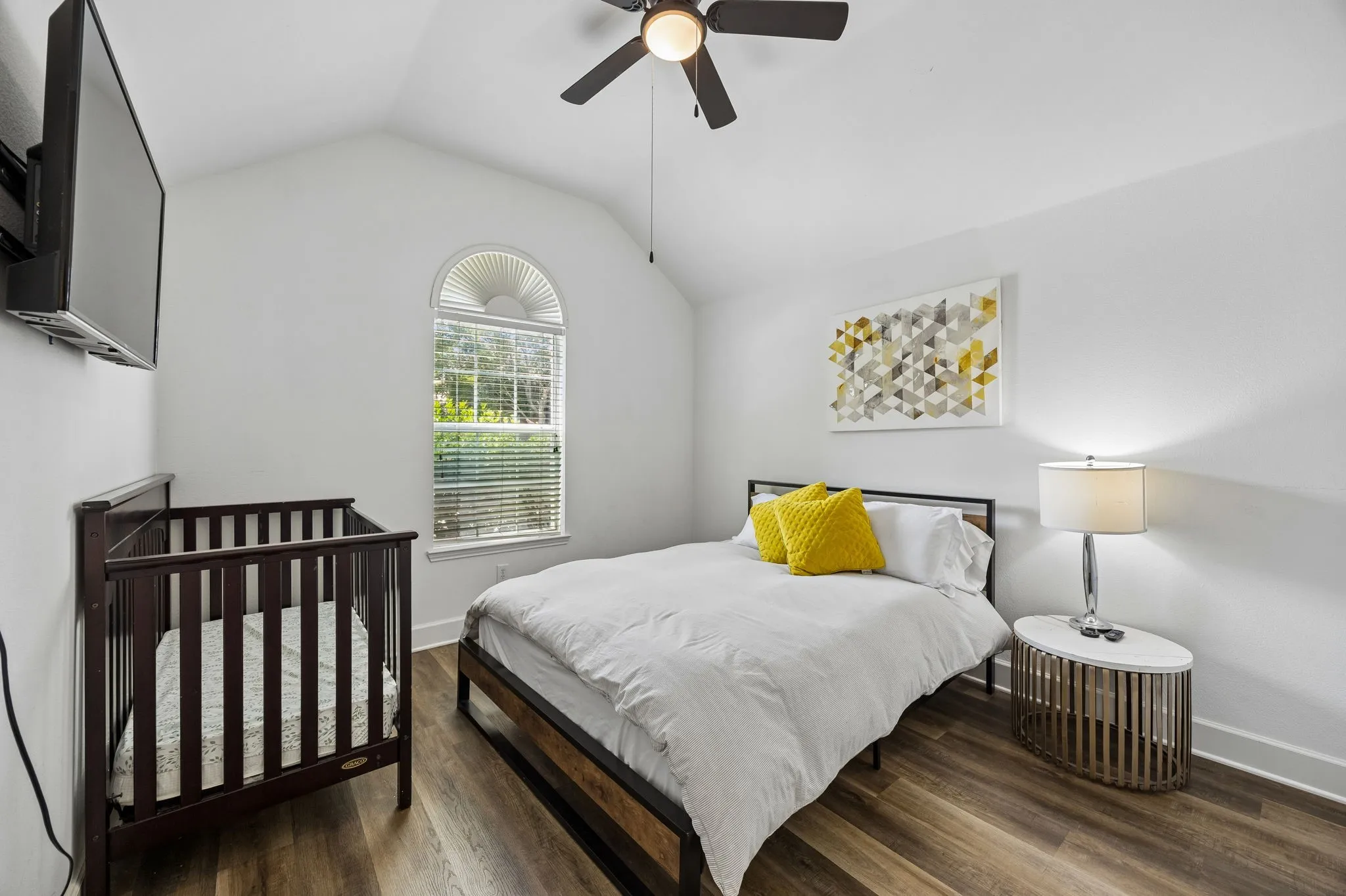 Vaulted ceiling with a ceiling fan, arched window with horizontal blinds, wood-finish flooring, and white walls