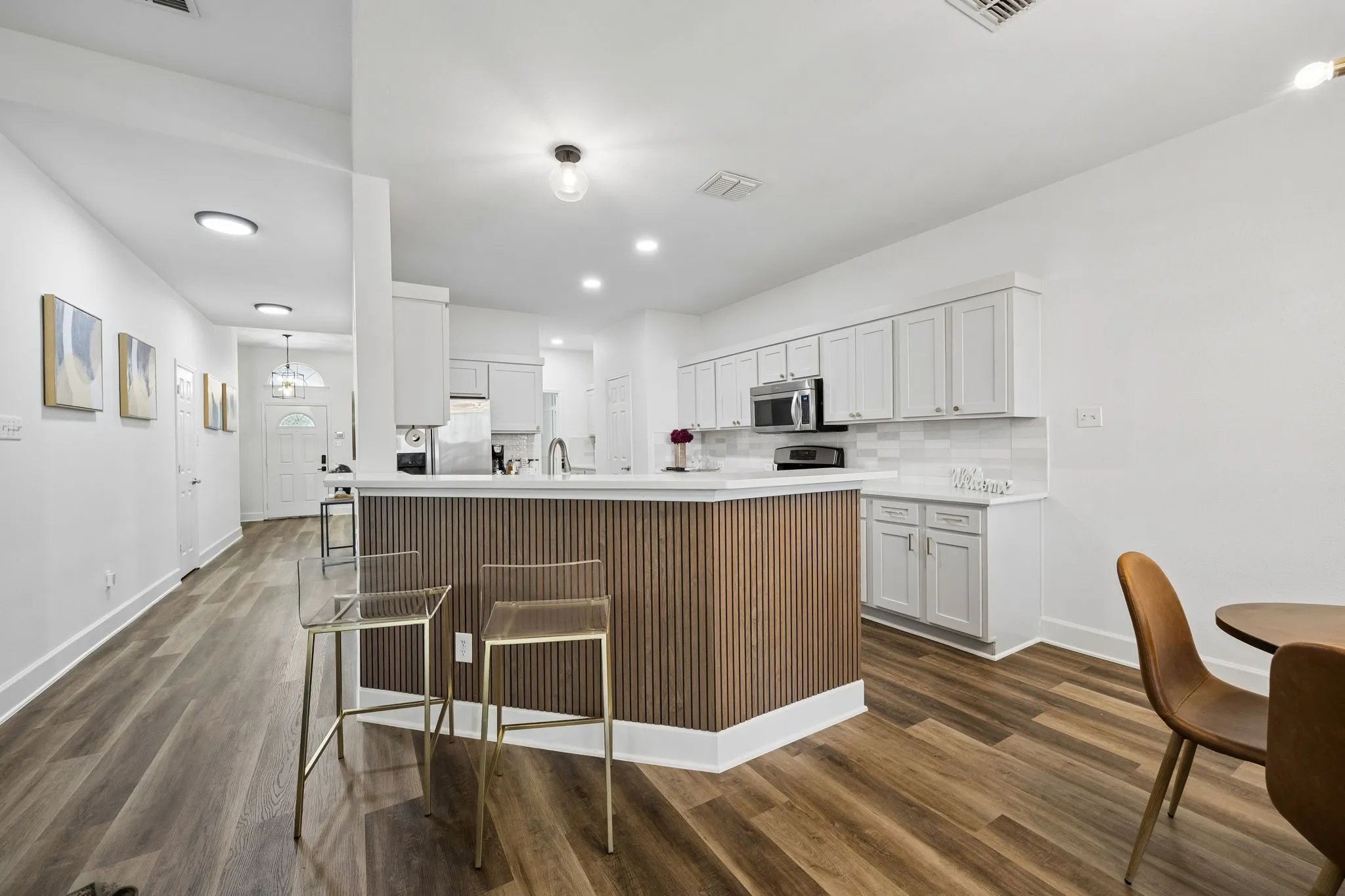 Kitchen featuring an island with wood-finish paneling, light-toned cabinetry, stainless steel appliances, and a tile backsplash