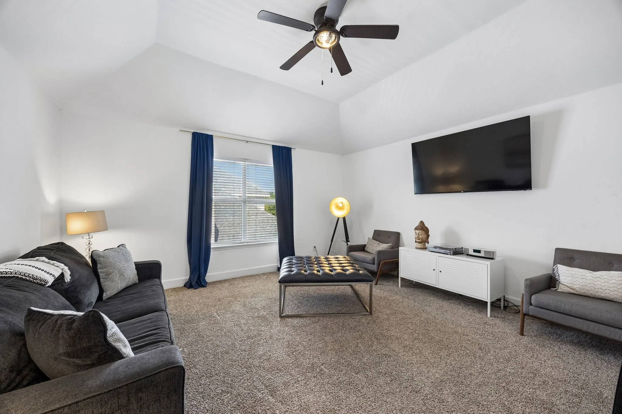 Vaulted ceiling with a ceiling fan, wall-mounted television, white built-in console, and a window with blinds