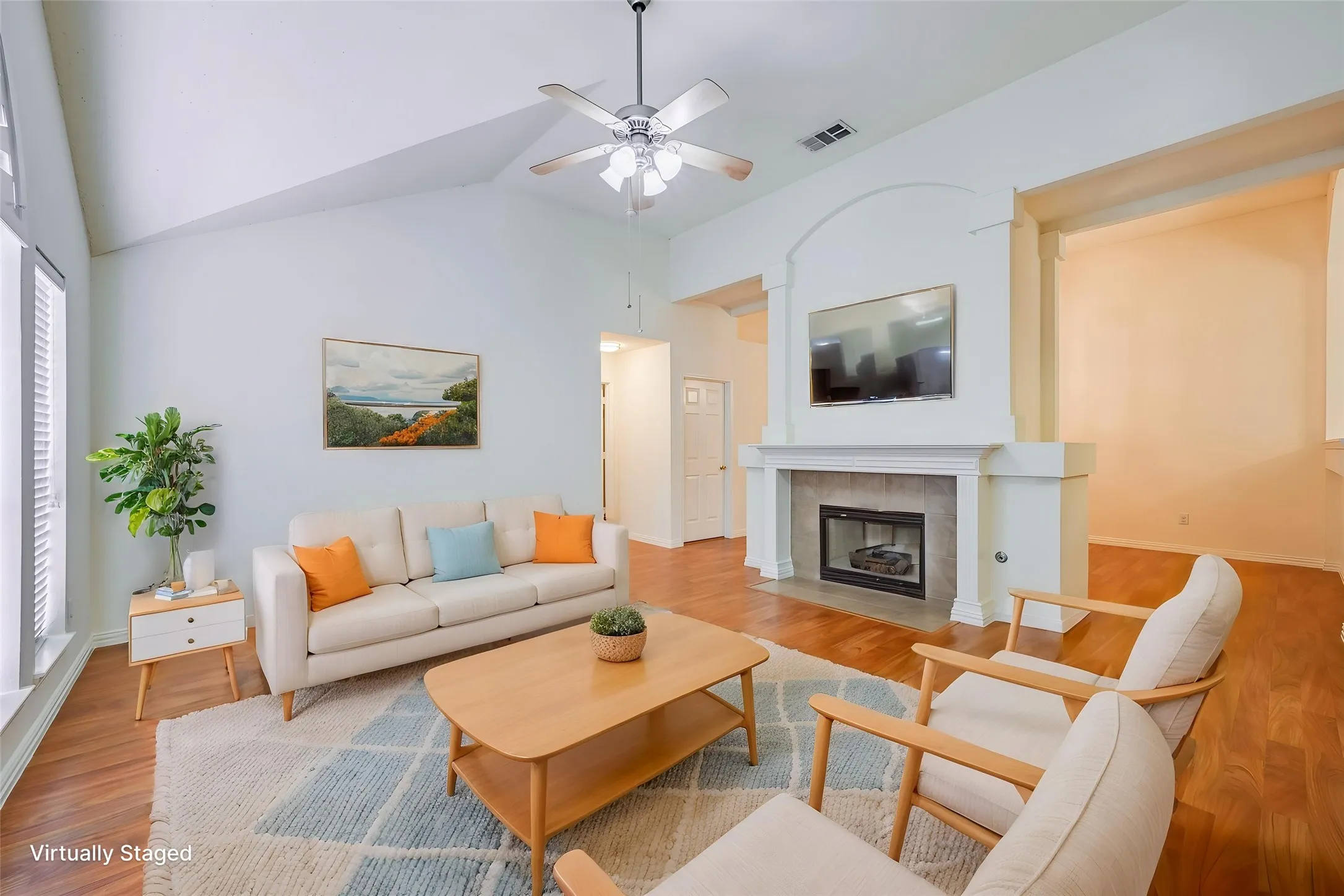 Vaulted ceiling, wood-finish flooring, fireplace with stone surround, ceiling fan, and large window