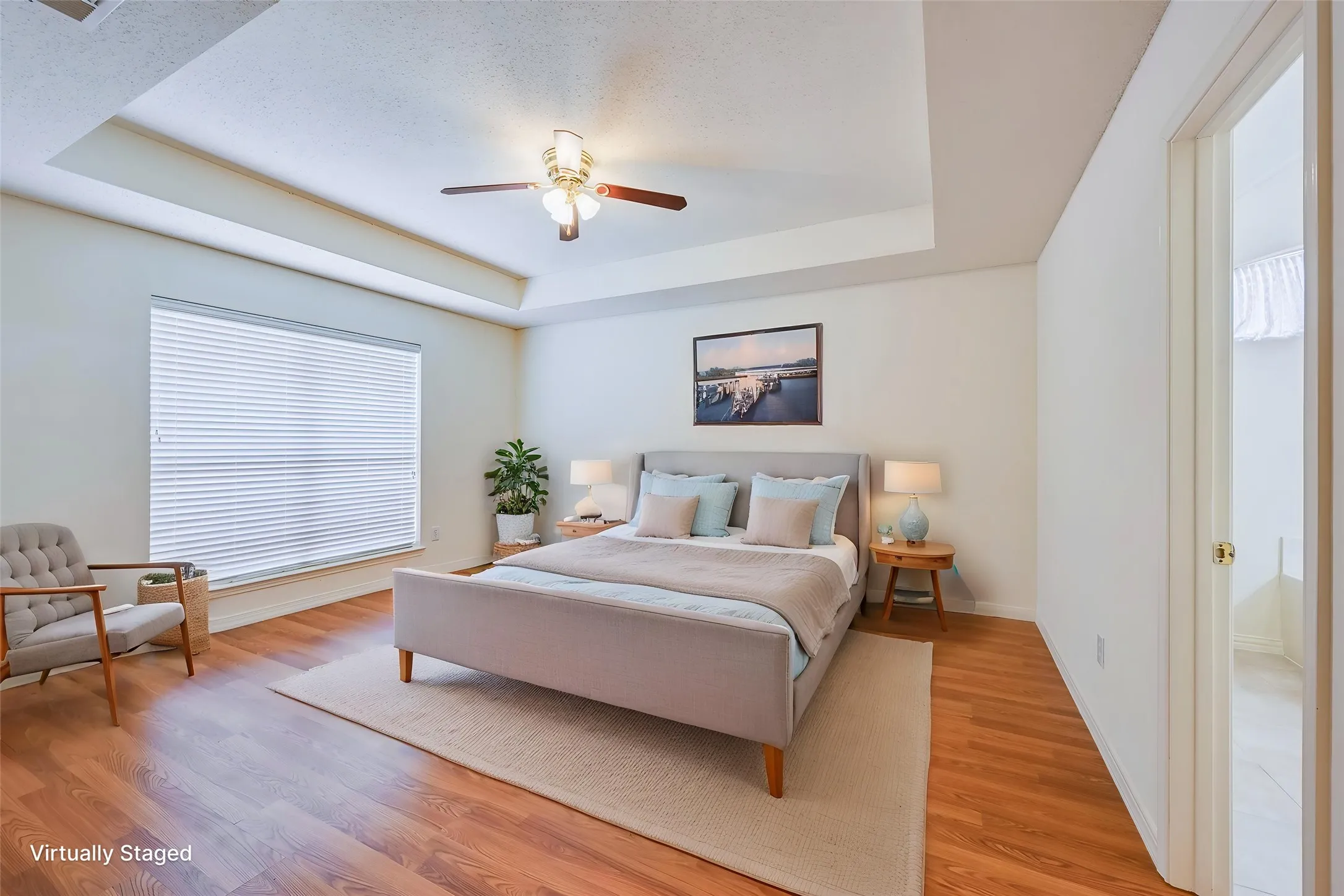 Tray ceiling with a ceiling fan, wood-finish flooring, and a large window with blinds